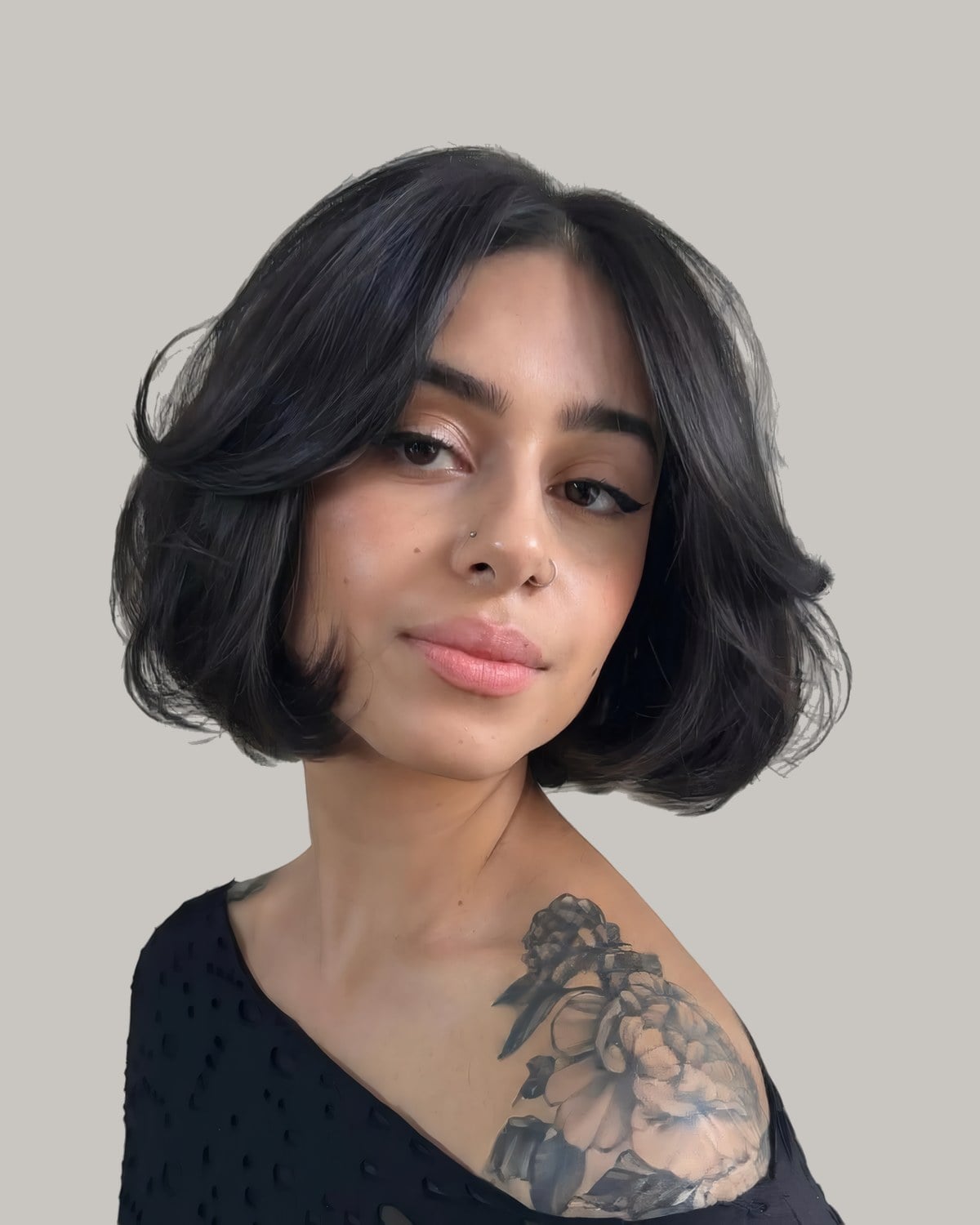 Woman with a tattoo on her shoulder and a rounded black chin-length bob with short bangs