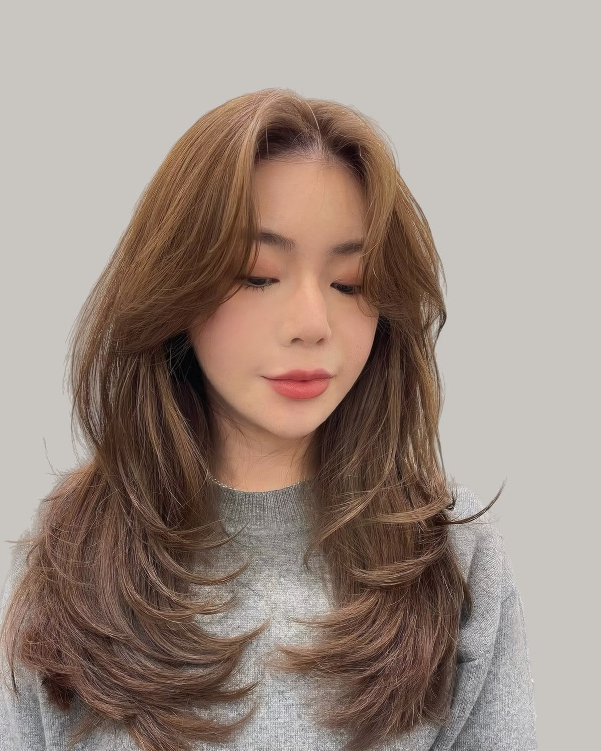 Woman with long, straight light brown hair in feathered layers, eyes lowered