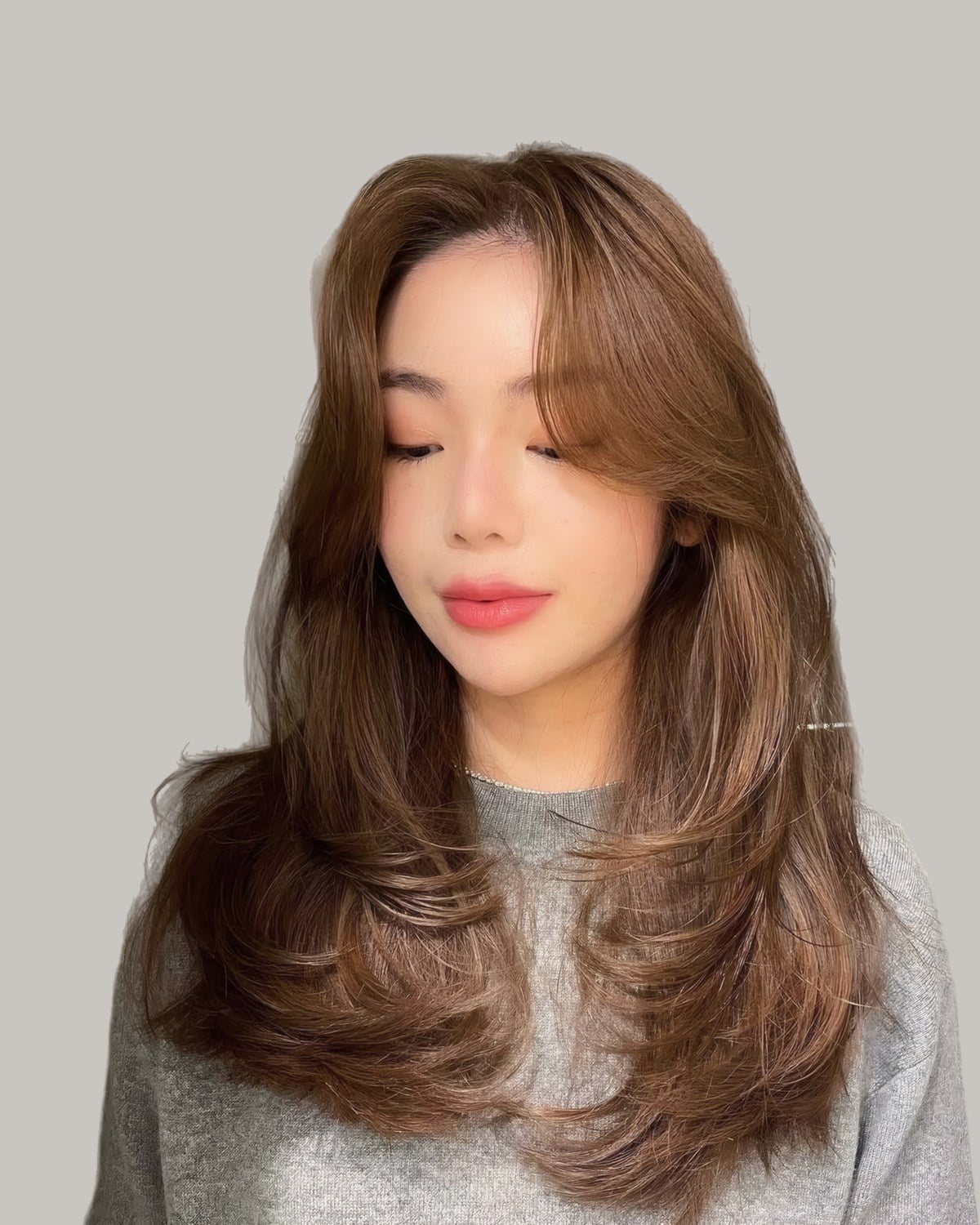Woman in a gray sweater with long, straight brown hair and wispy face-framing layers