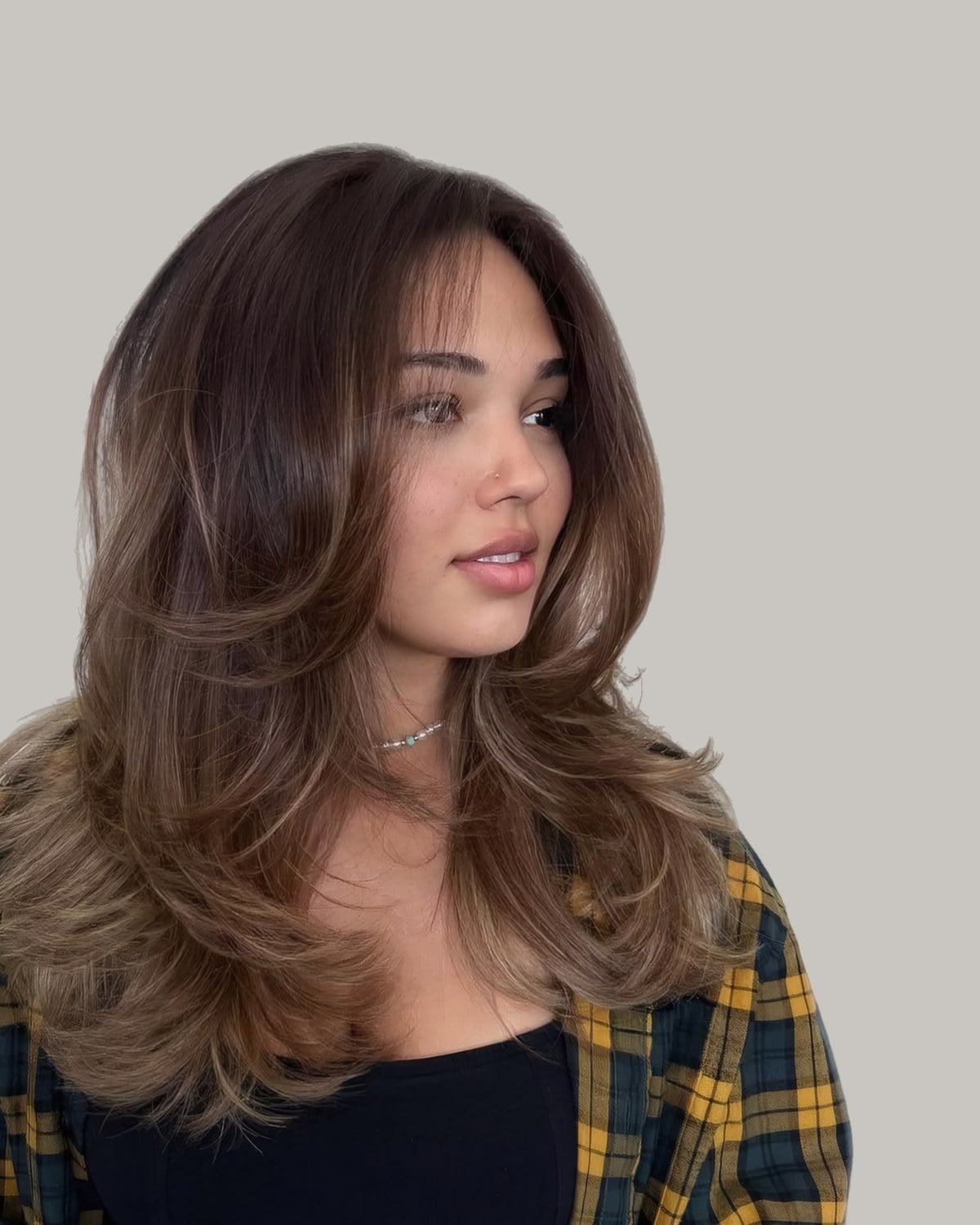 Woman in a plaid shirt with long brown hair and lighter ends, looking to the side