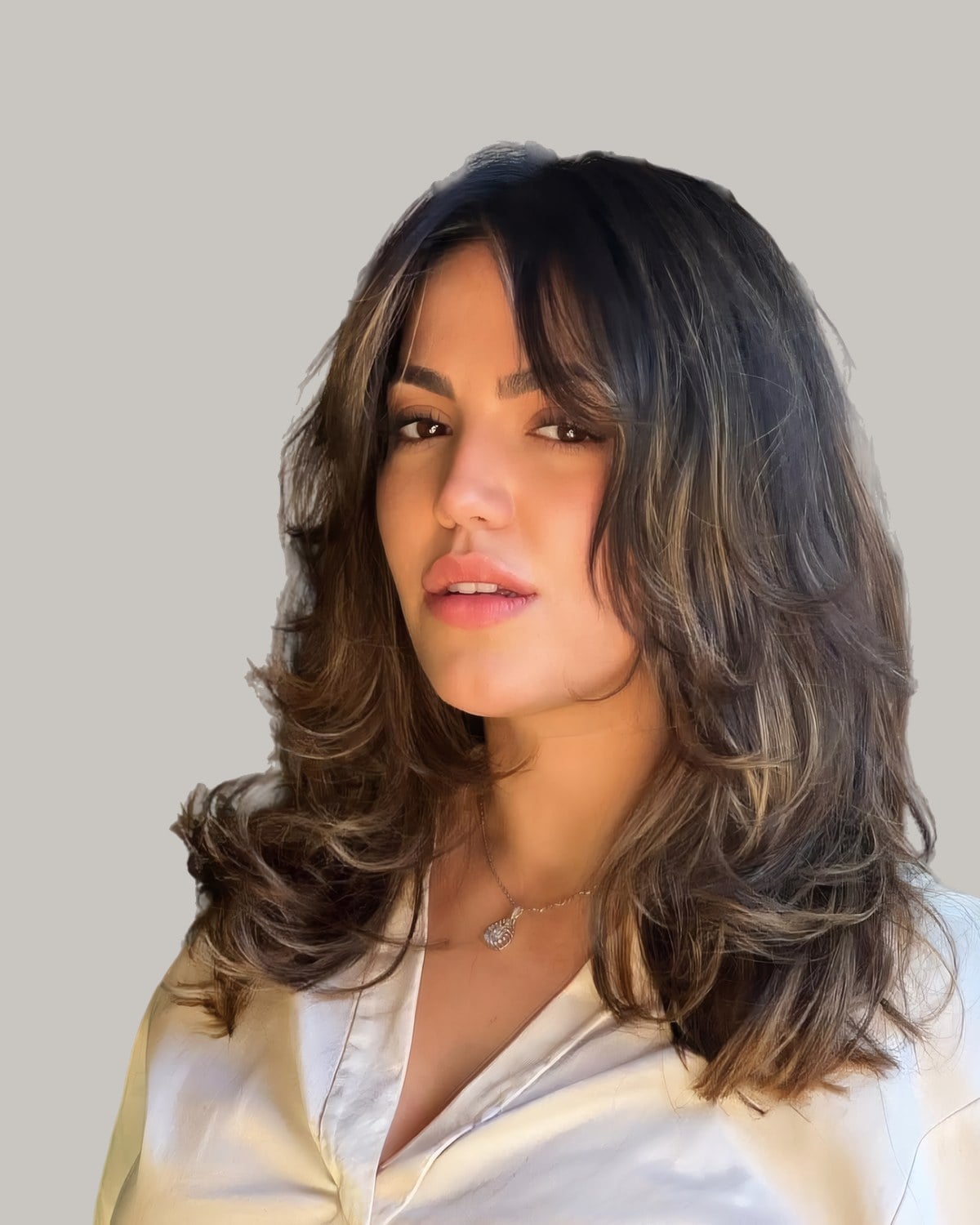 Woman in a white shirt with collarbone-length dark hair, wispy bangs and layers, looking down