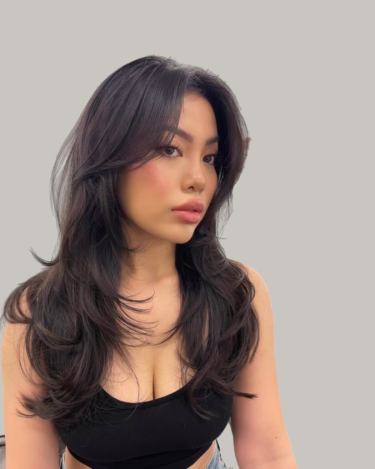 Woman with long black hair, curtain bangs and wispy face-framing layers