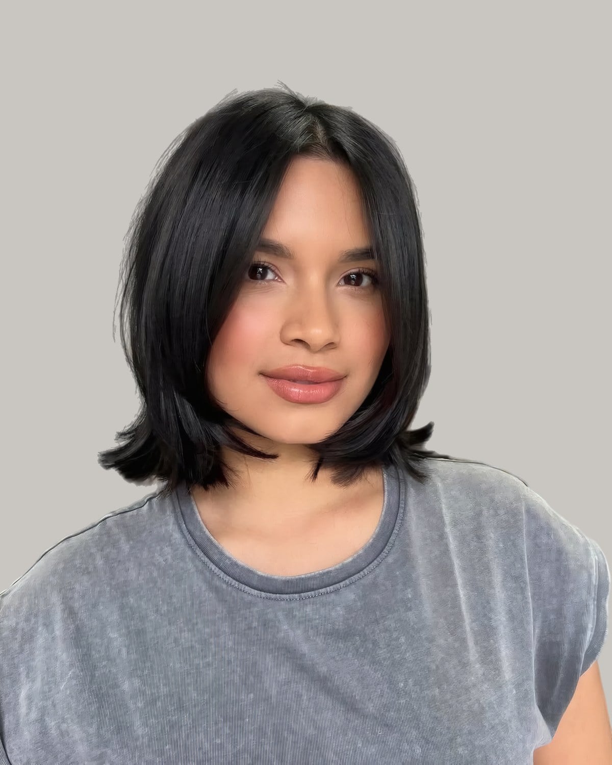 Woman in a gray T-shirt with a straight, shoulder-length black lob and a middle part
