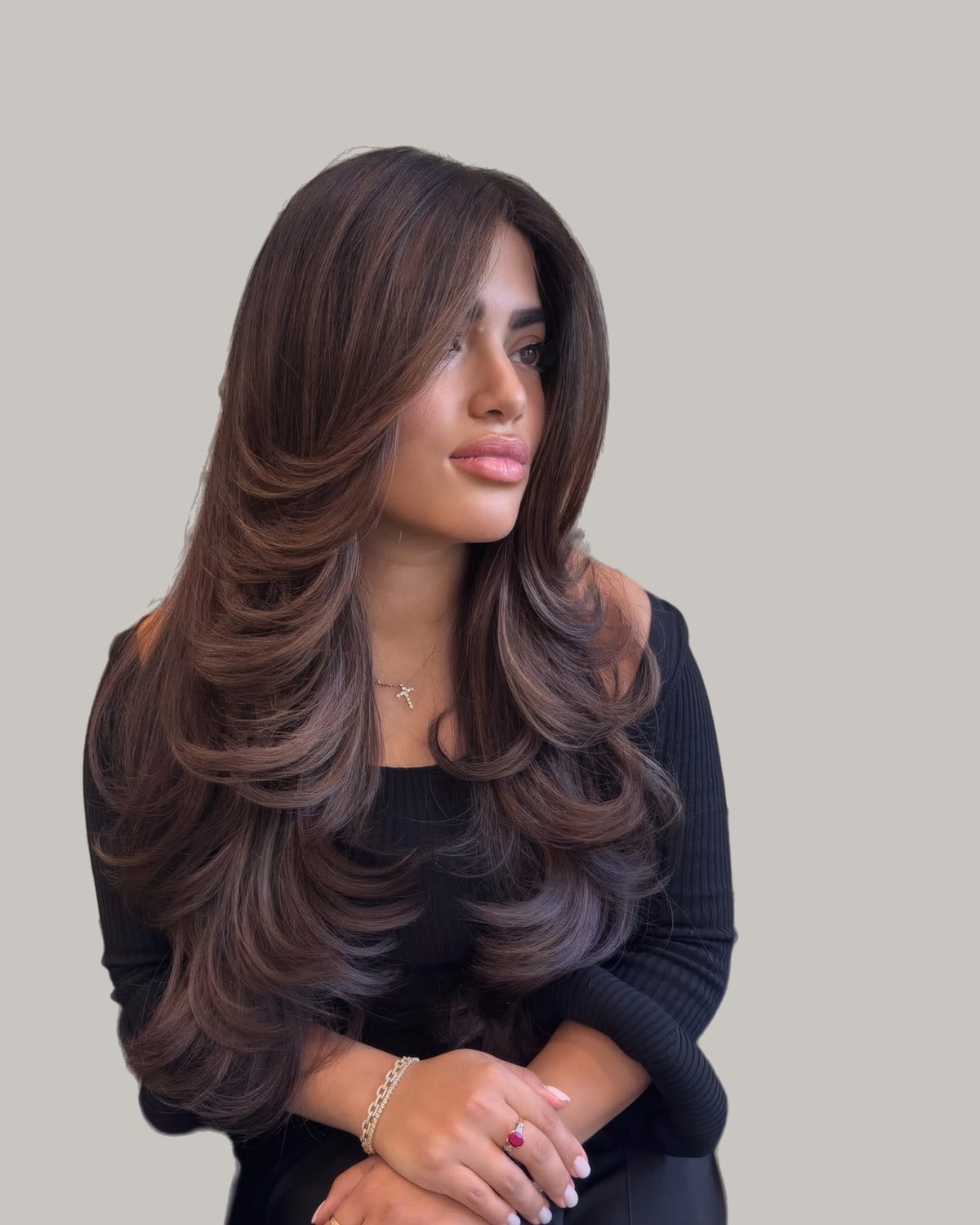 Seated woman in black with long, dark brown hair blown out in big face-framing curls