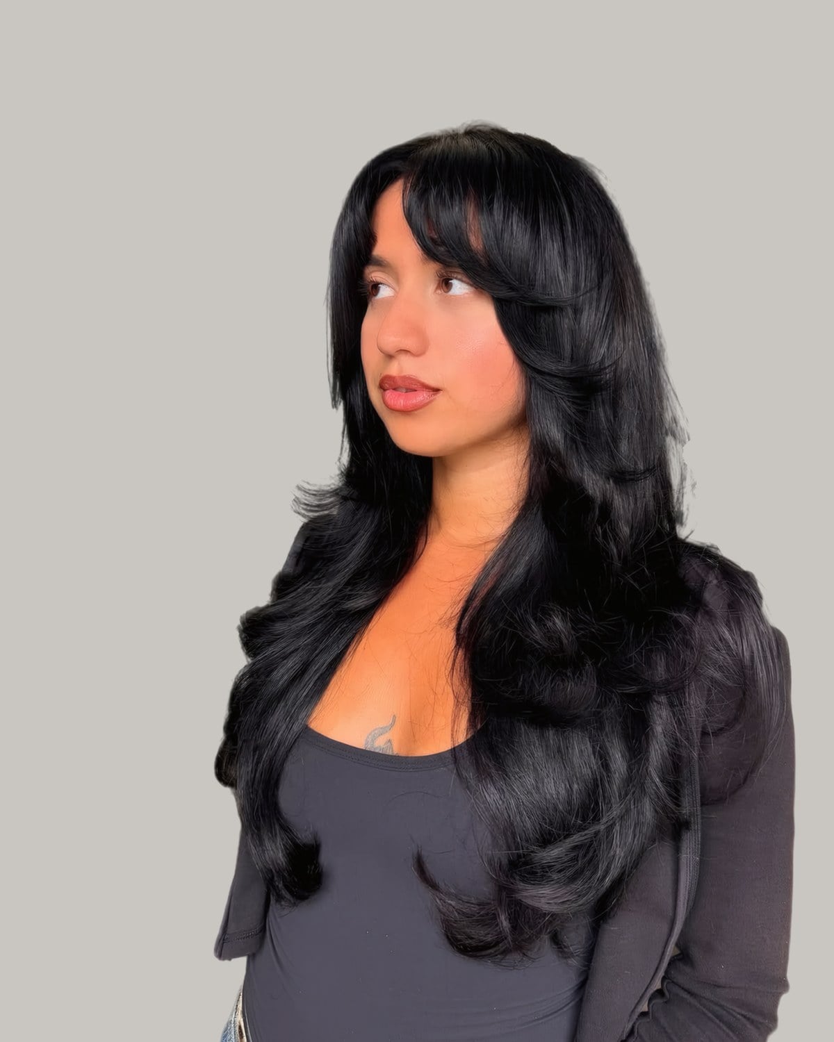 Woman looking to the side with long black hair, bangs and curled butterfly layers