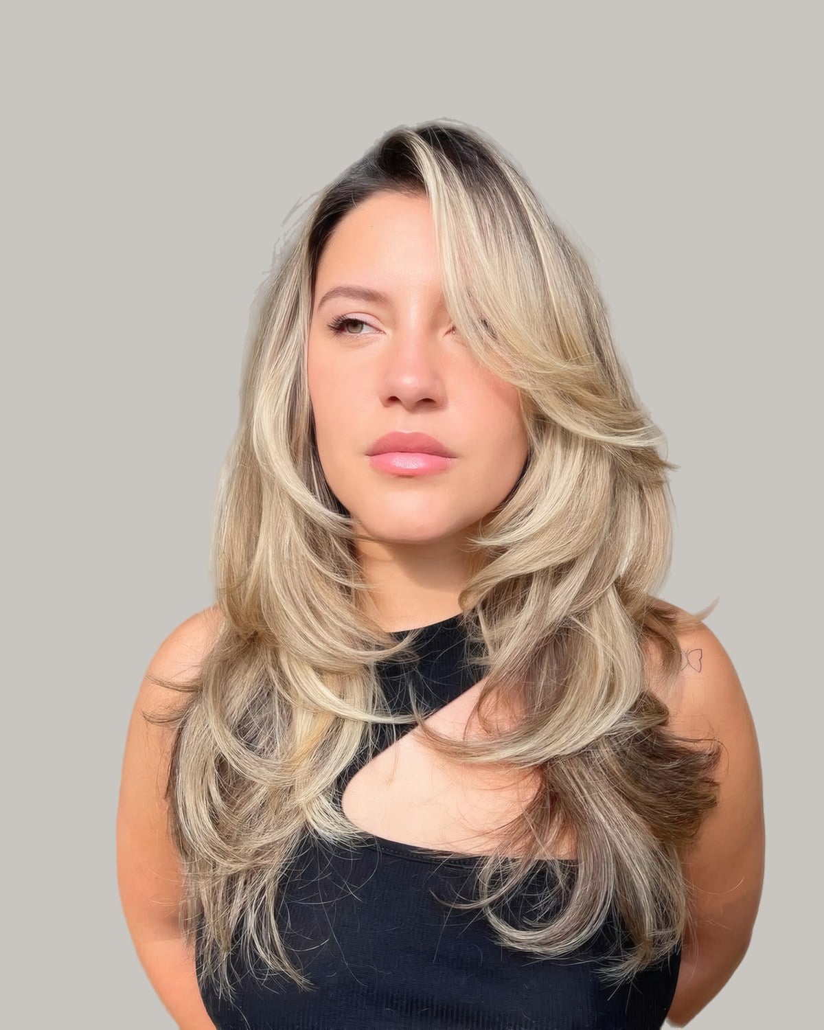 Woman with long ash blonde layers and a dark root, head tilted to one side