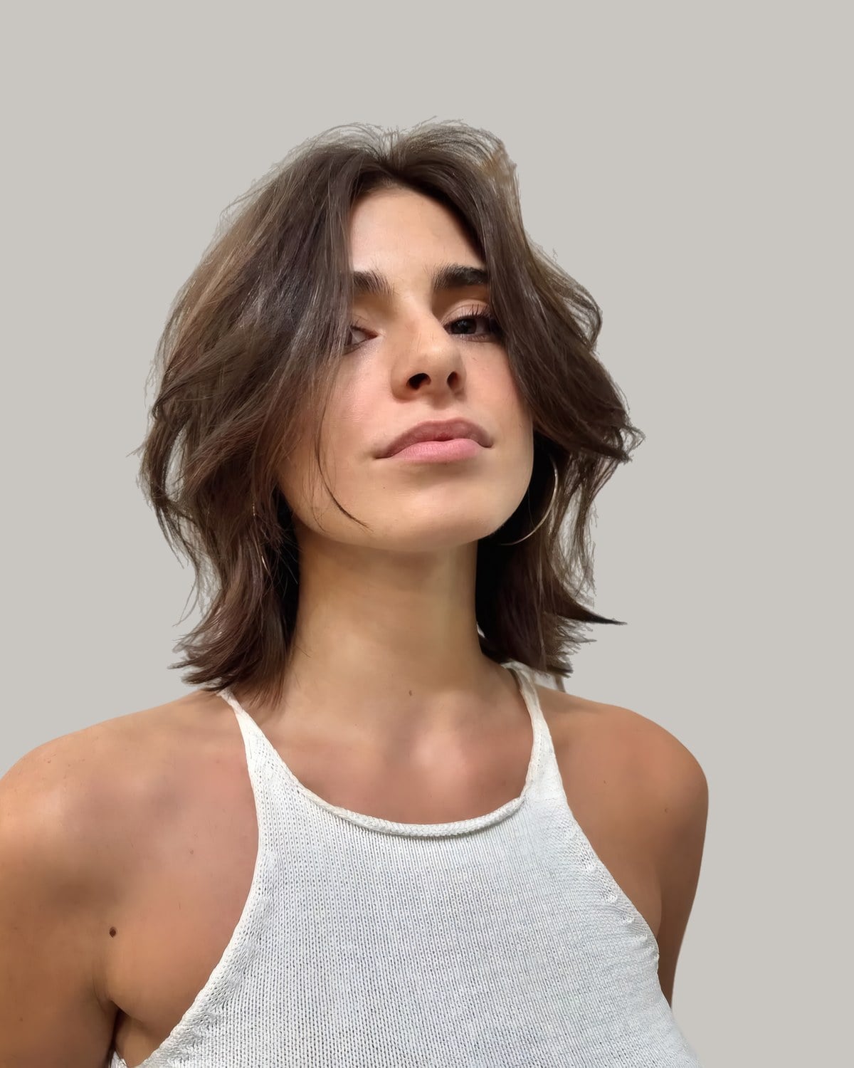 Woman with a messy brown butterfly cut that skims the shoulders, head tilted