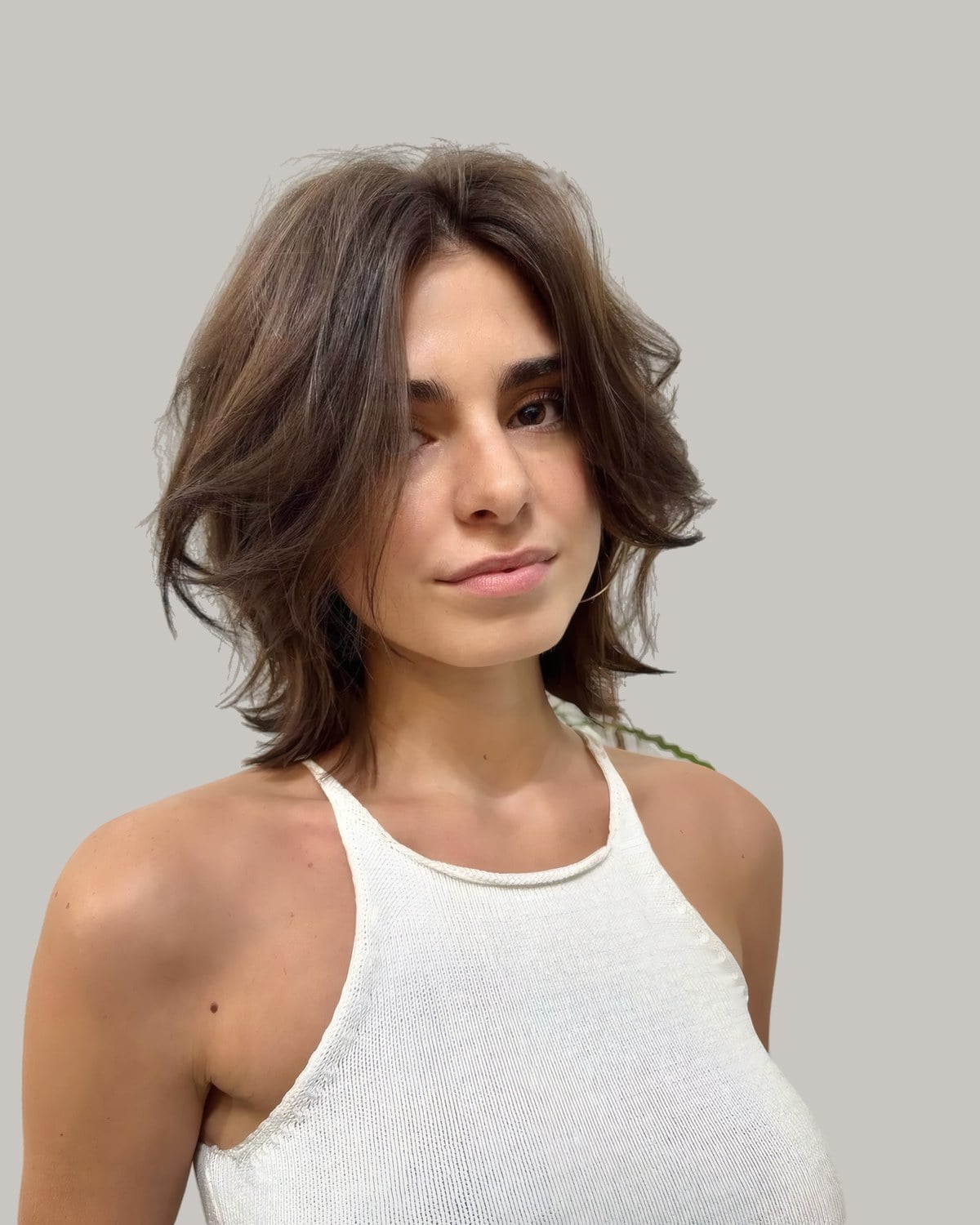 Woman in a white halter top with a tousled brown cut just above the shoulders