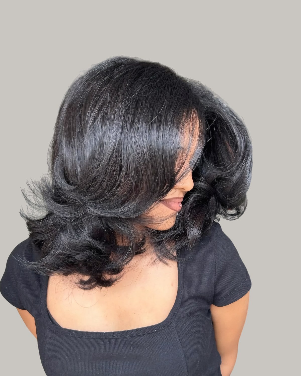 Woman with black shoulder-length hair in bouncy layers, face turned away