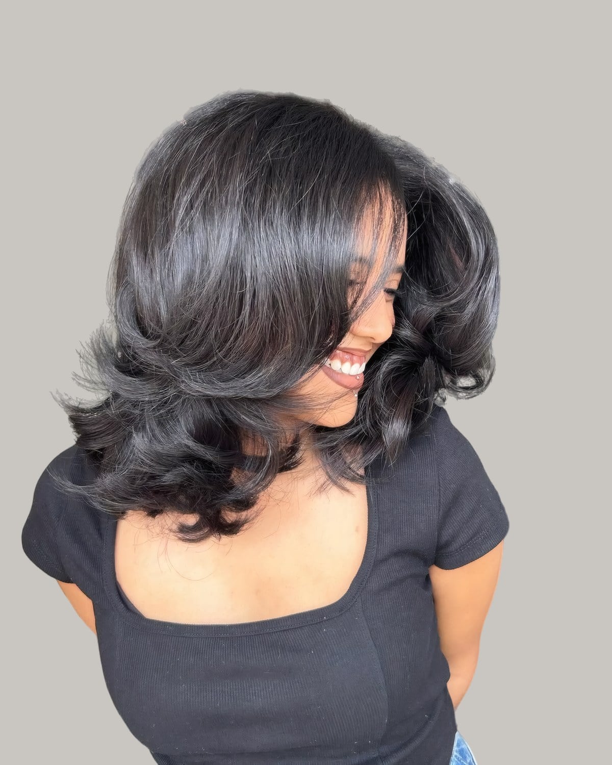 Woman in a black top laughing, glossy black shoulder-length hair flipped out in layers