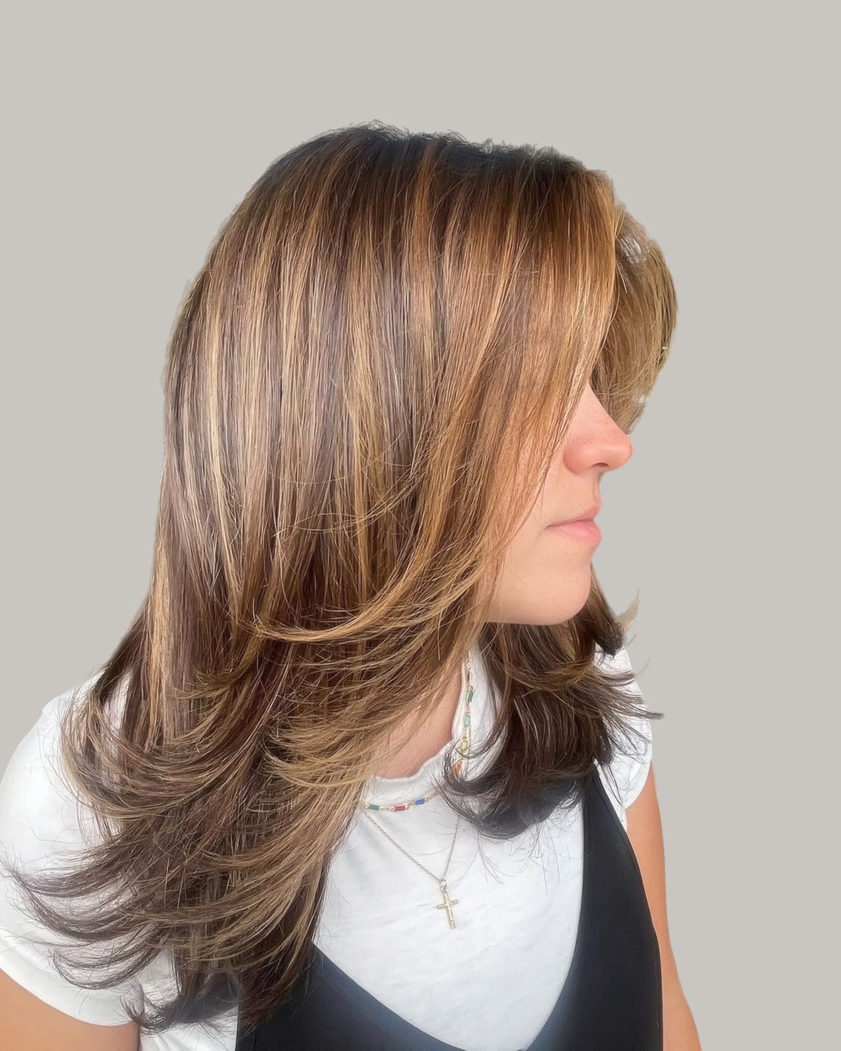 Woman in profile with long, straight hair and caramel pieces through the layers