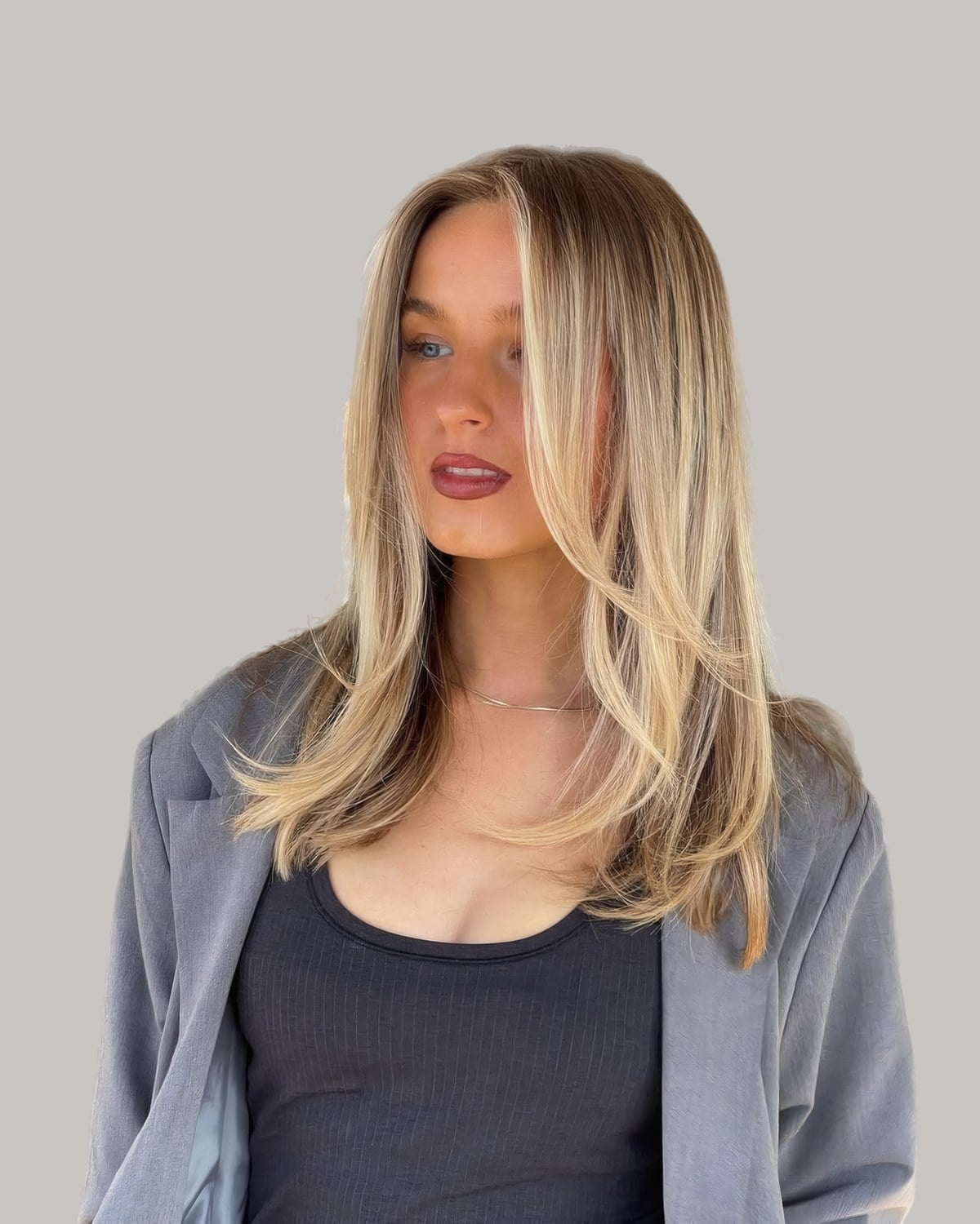 Woman in a gray blazer with long, straight blonde hair and face-framing layers