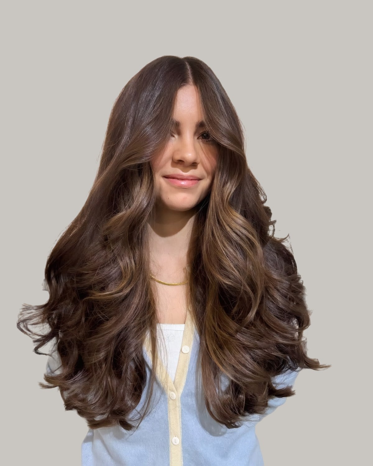 Smiling woman in a cream cardigan with very long brunette waves and a middle part