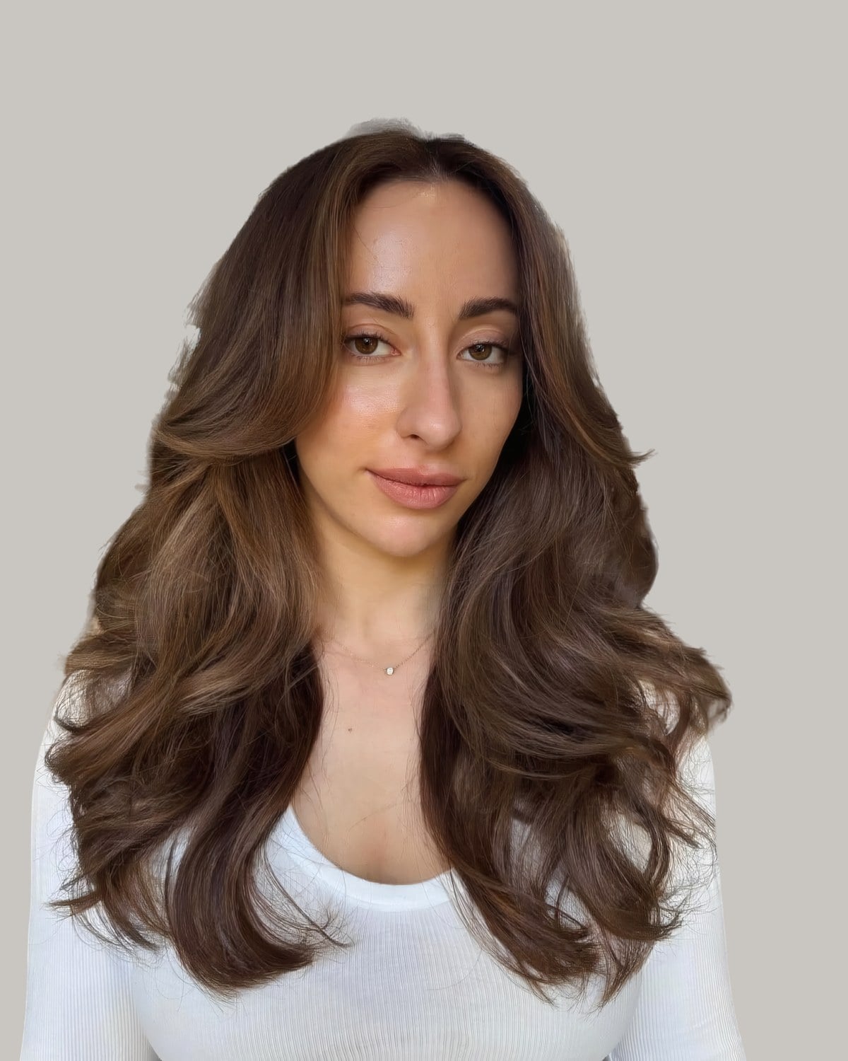 Woman in a white top with long, soft brunette waves and face-framing layers