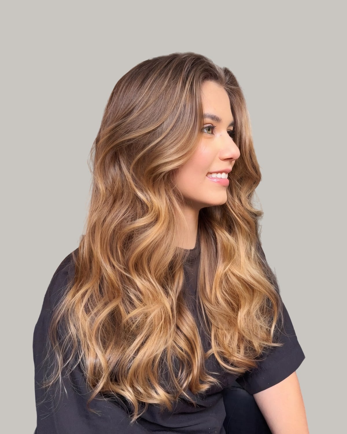 Woman in profile smiling, long caramel and honey waves over a black top