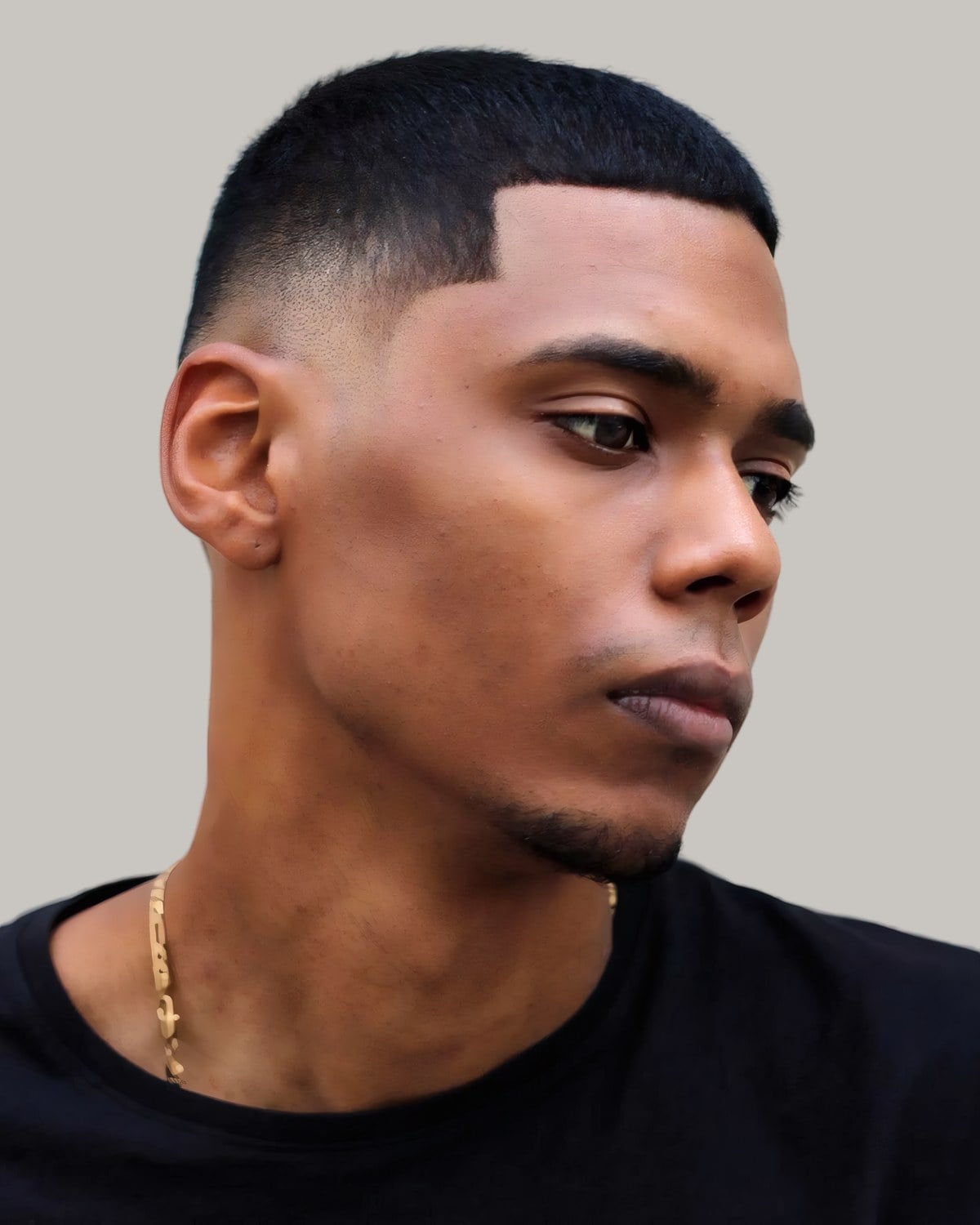 Man with a buzz cut and a sharp line-up, seen in profile in a barber's cape