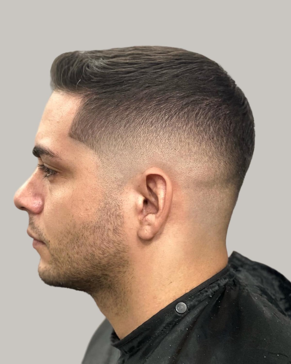 Man with stubble, a long buzz cut and a mid skin fade, seen in profile