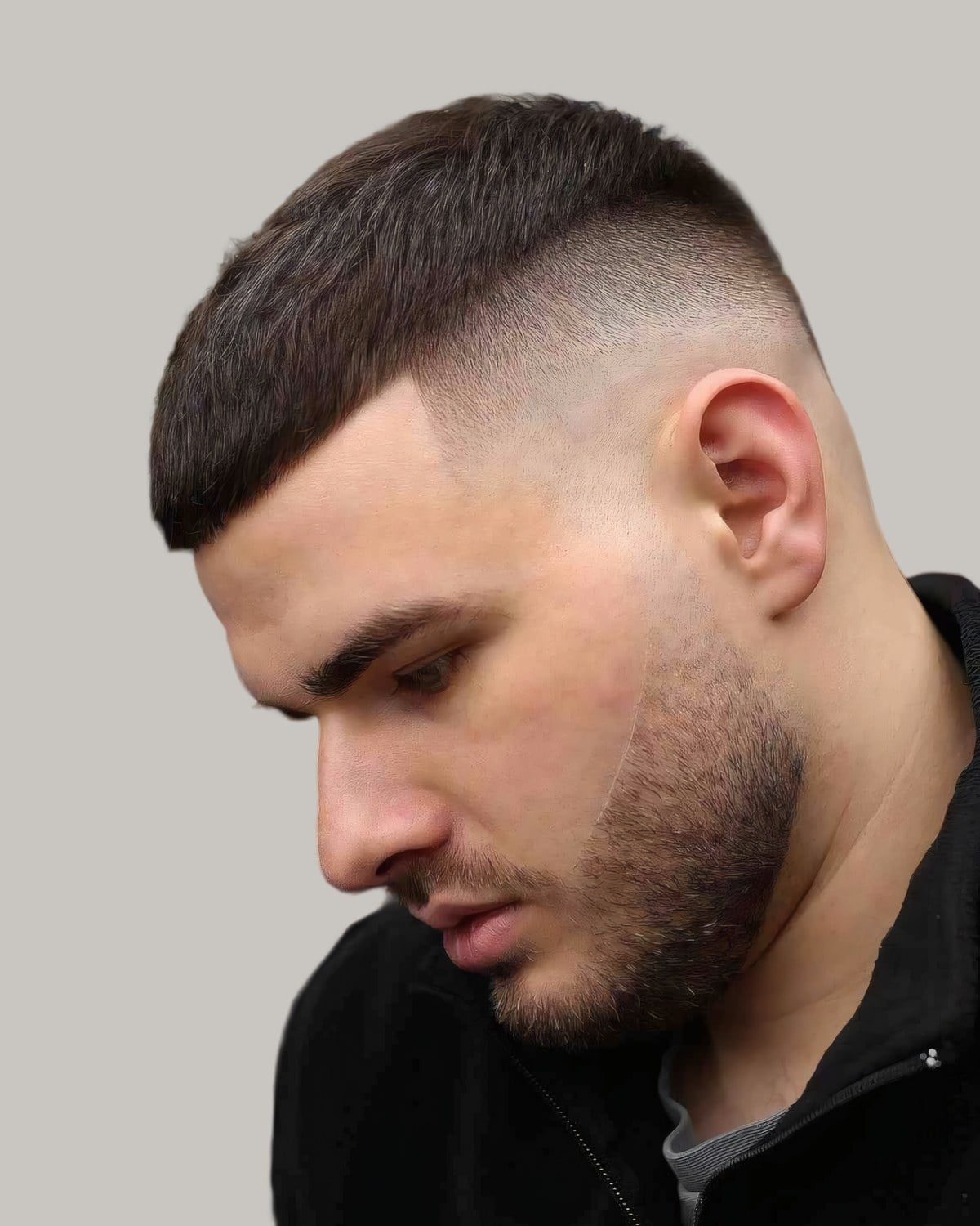 Man with a military buzz cut and a high skin fade, looking down