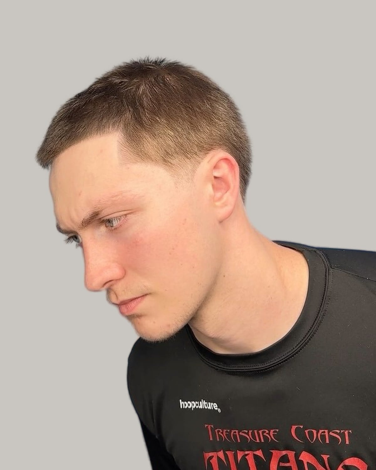 Young man with a number 10 buzz cut and a low taper fade, looking down to one side