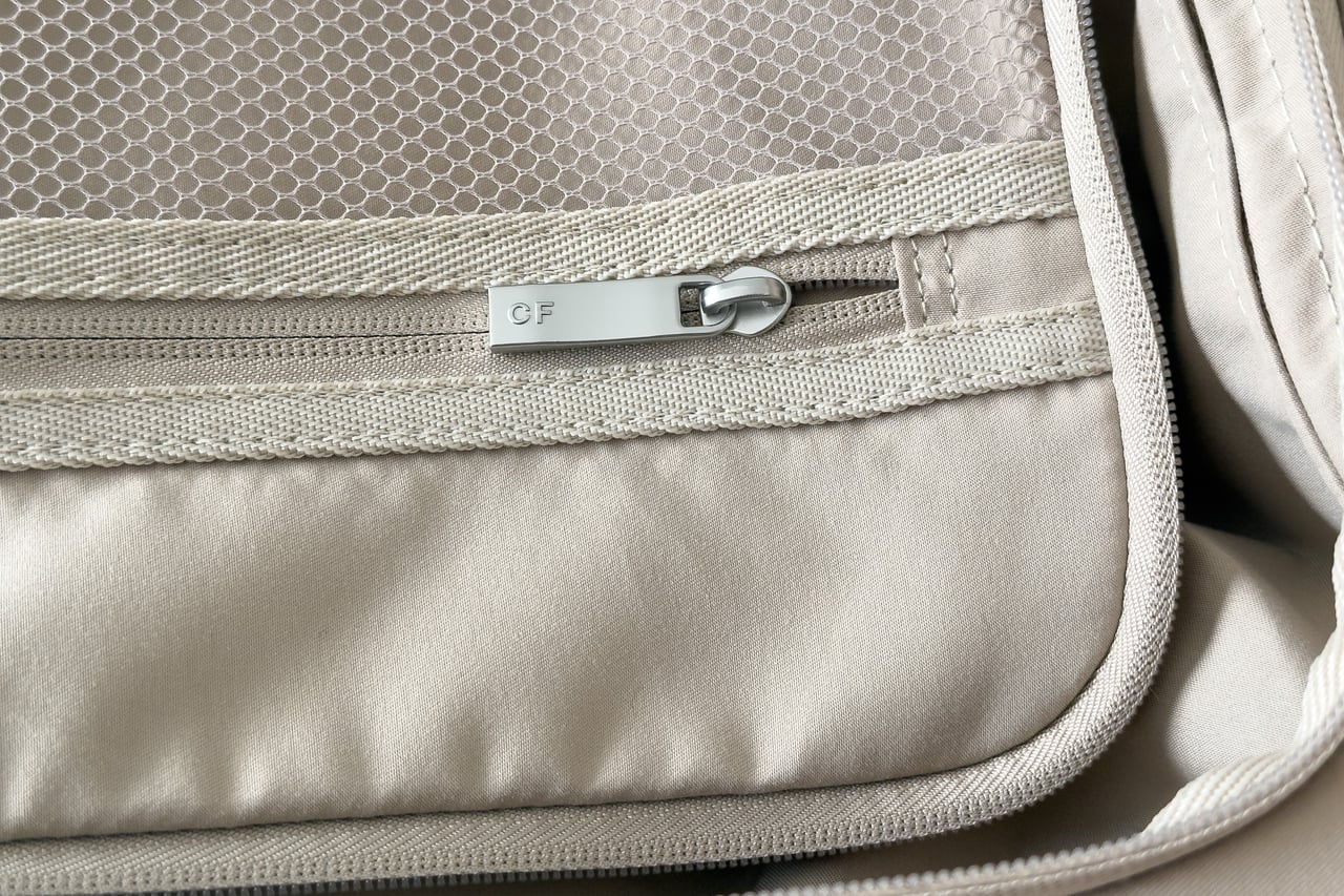Two CF zip pulls on the open Carl Friedrik suitcase above a leather side handle - Luxe Digital