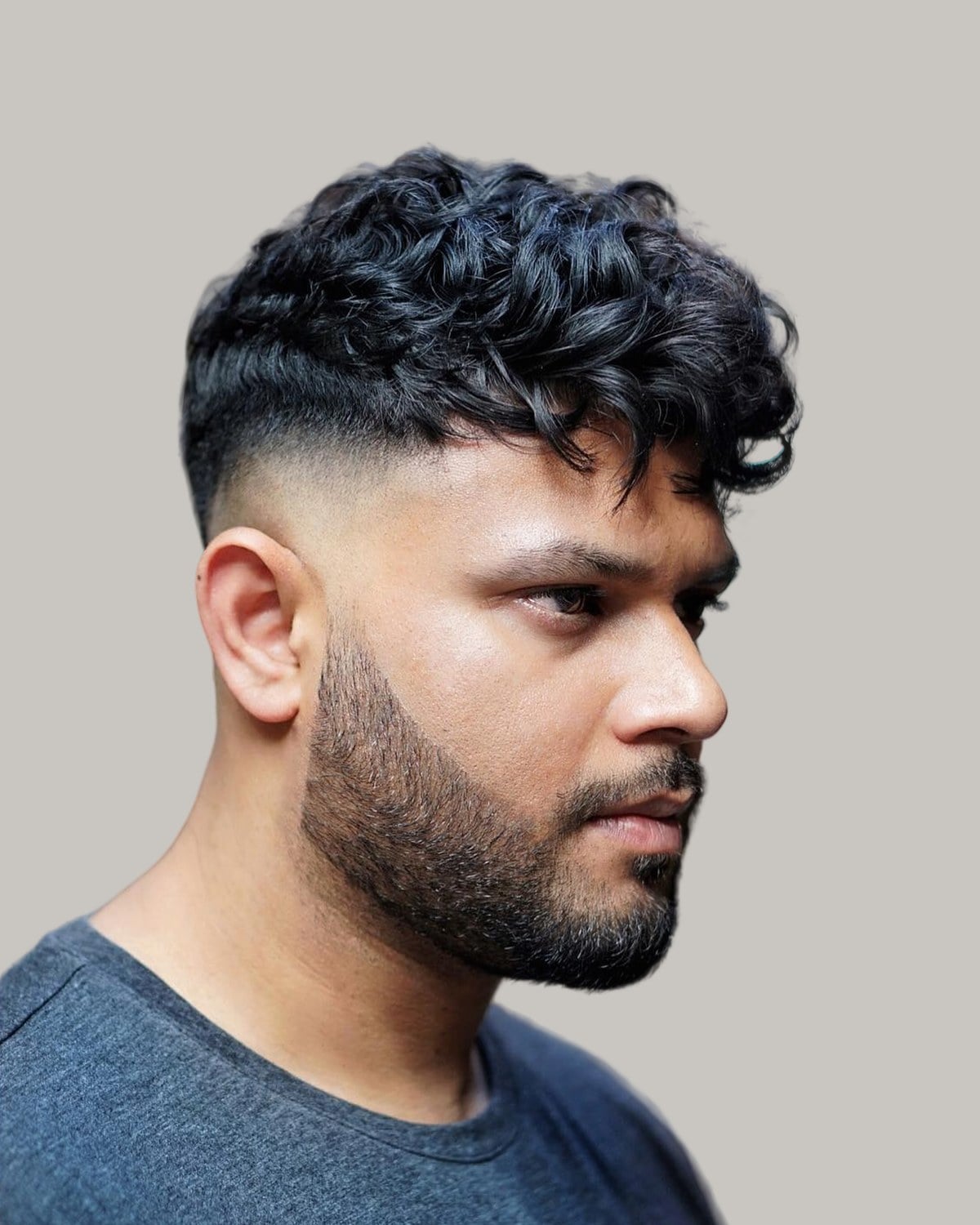 Bearded man with a curly crew cut and a fade, seen at an angle
