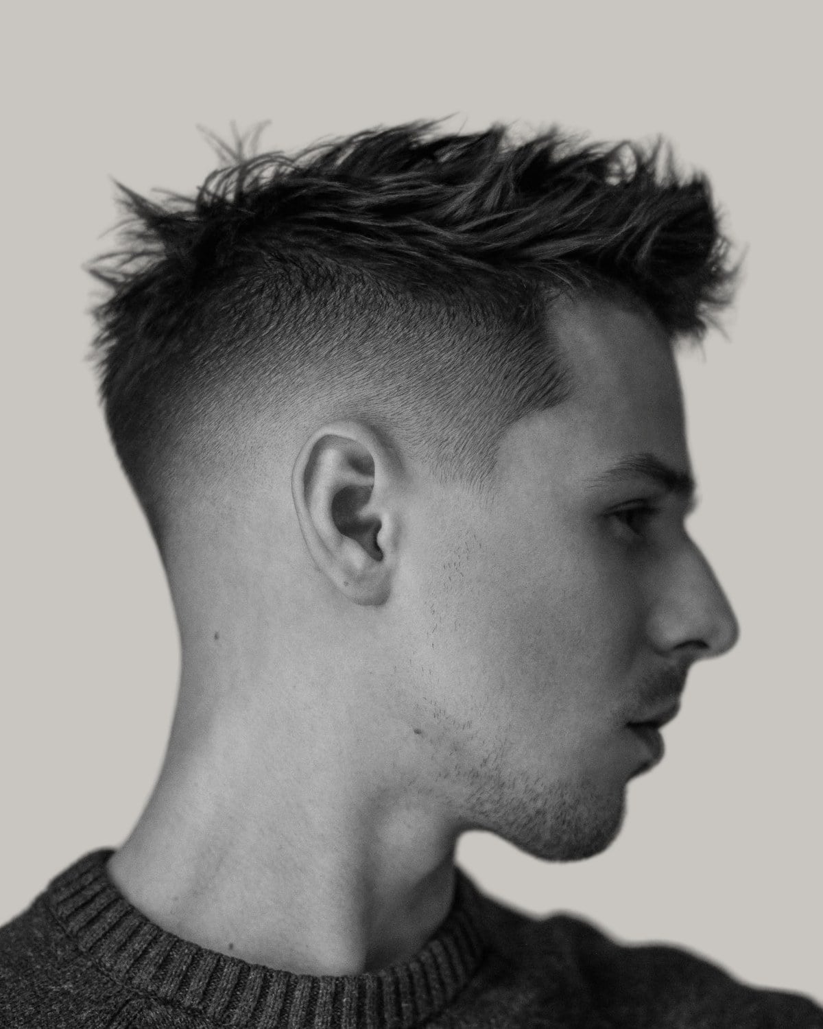 Man with a spiky crew cut and a high fade, seen in profile in black and white