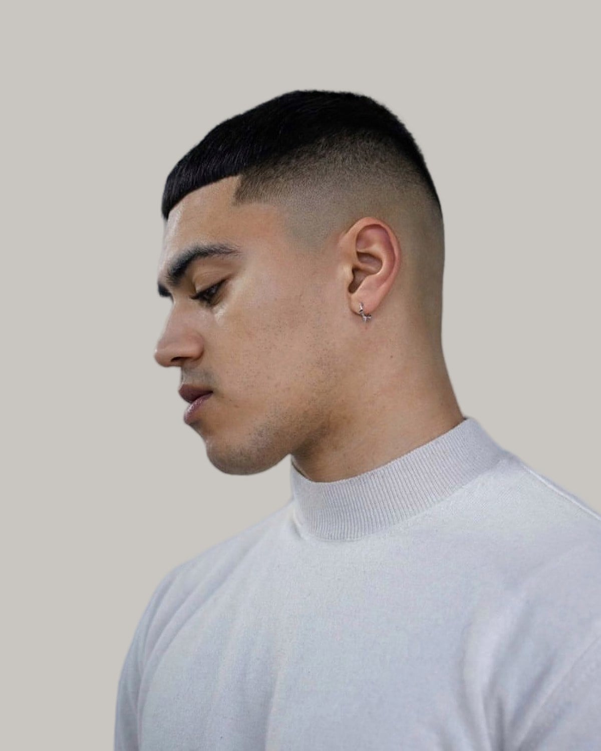 Man with a high and tight haircut, seen in profile looking down