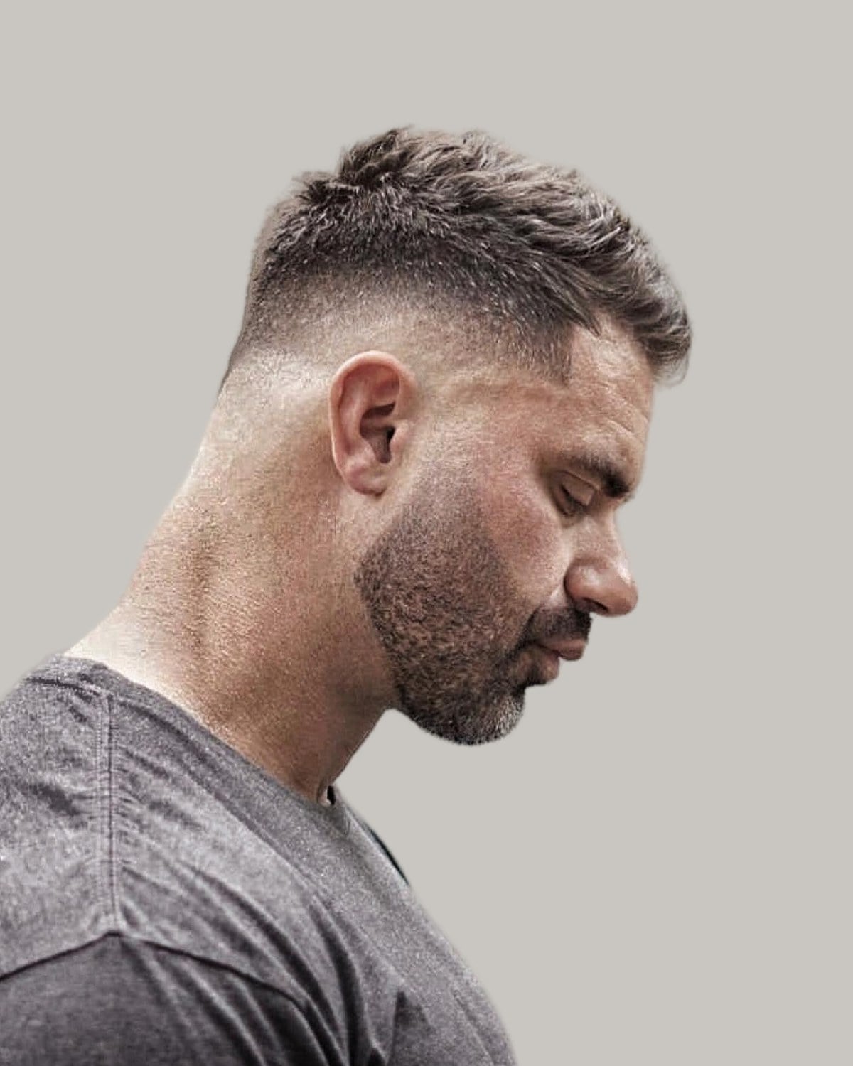 Man with a modern crew cut and a stubble beard, seen in profile looking down