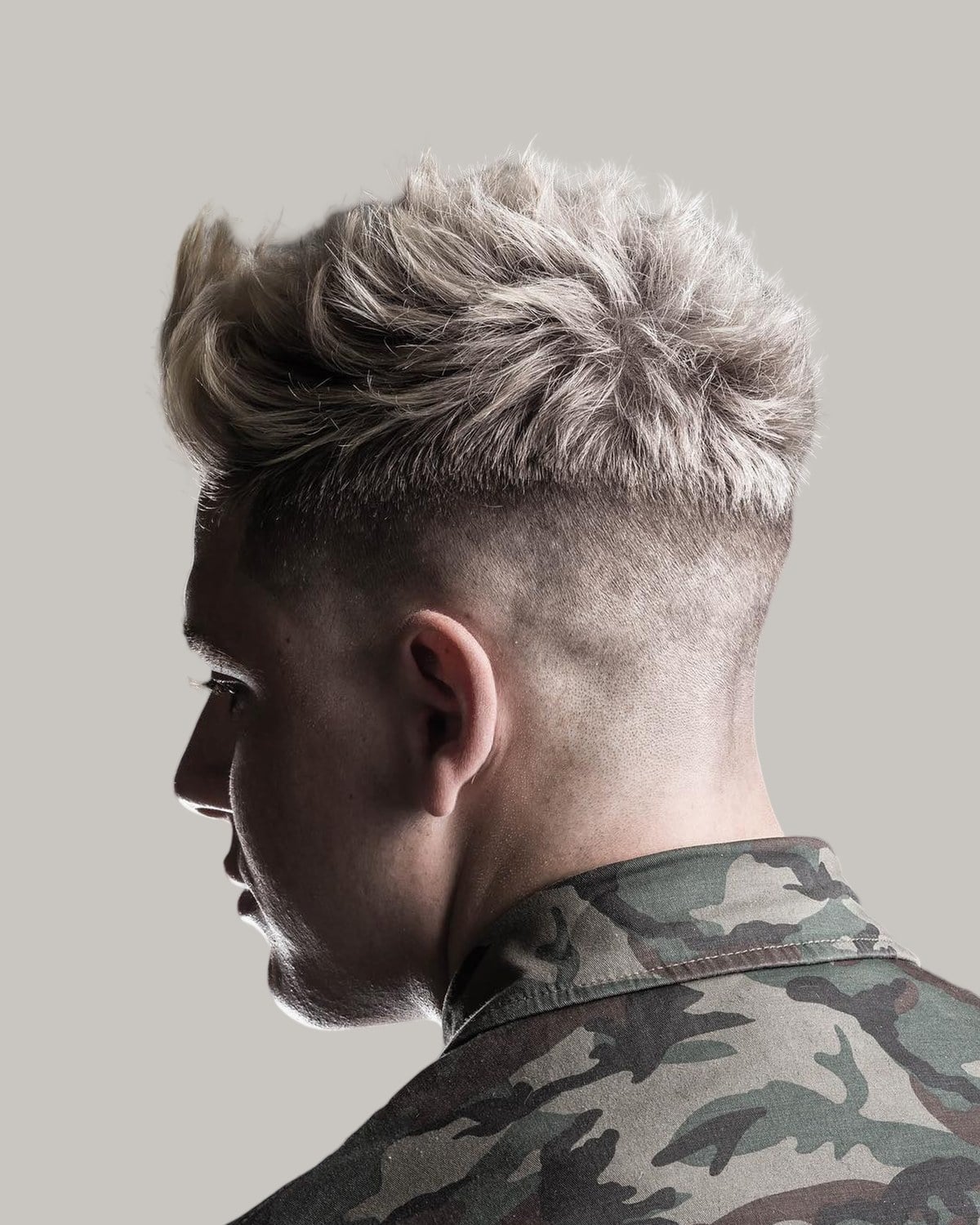 Man with a platinum textured crew cut and a high fade, seen from behind at an angle