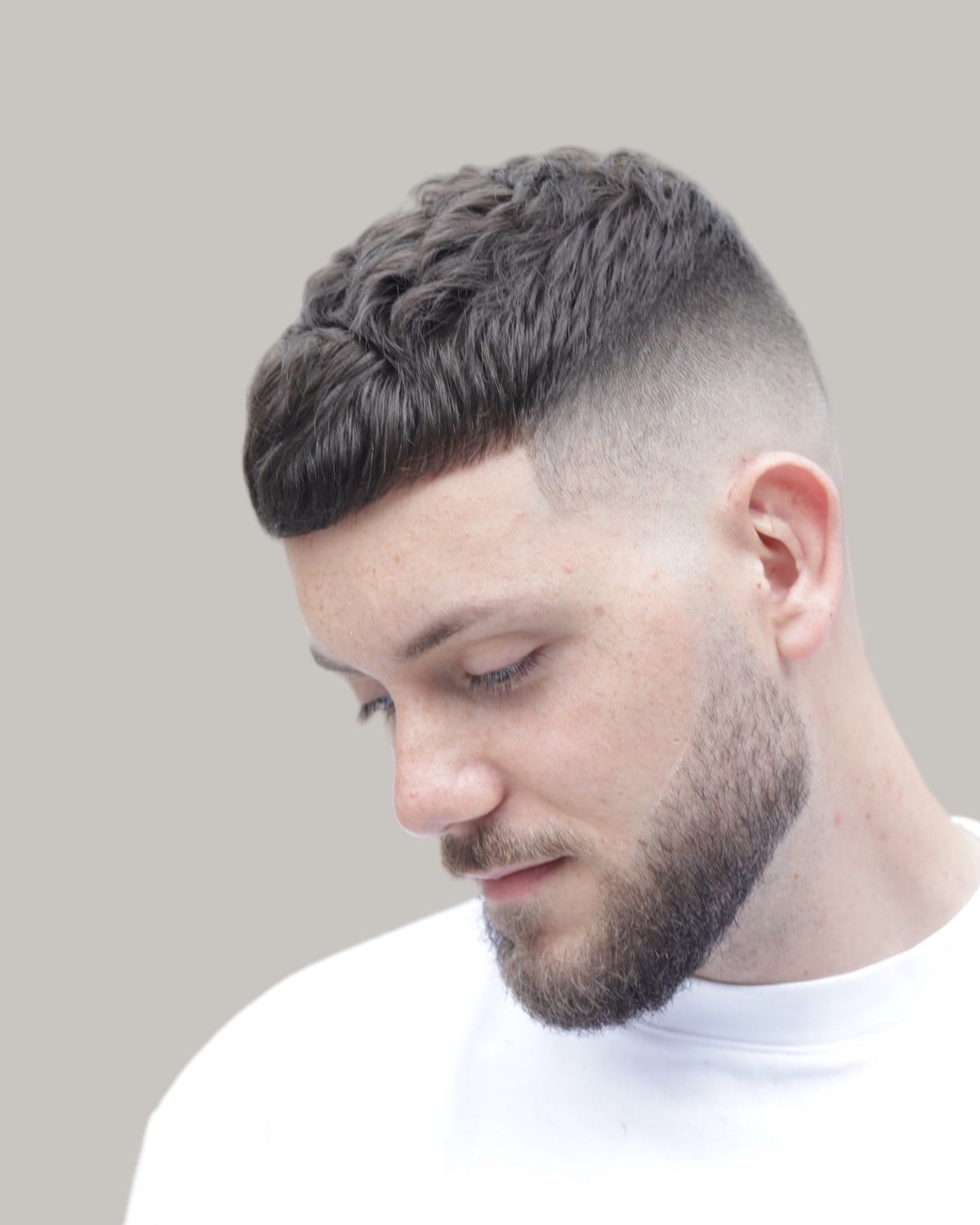 Bearded man with a textured crew cut and a skin fade, seen at an angle looking down