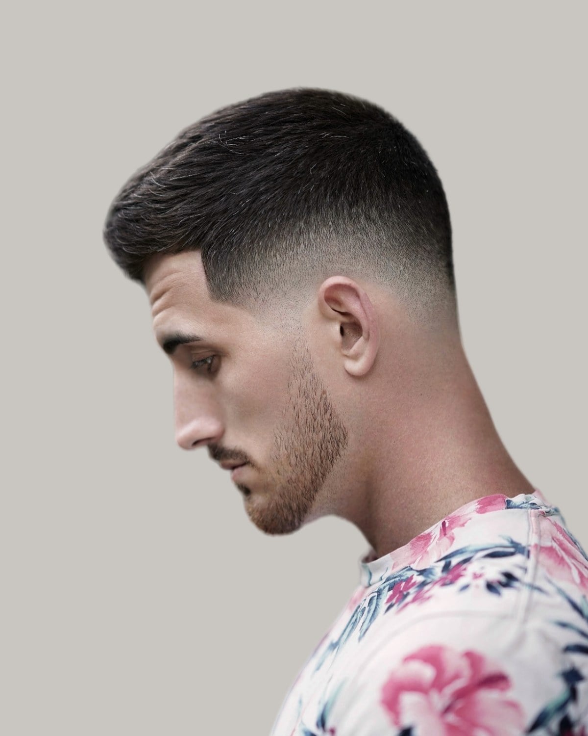 Man with a crew cut and a taper fade, seen in profile looking down