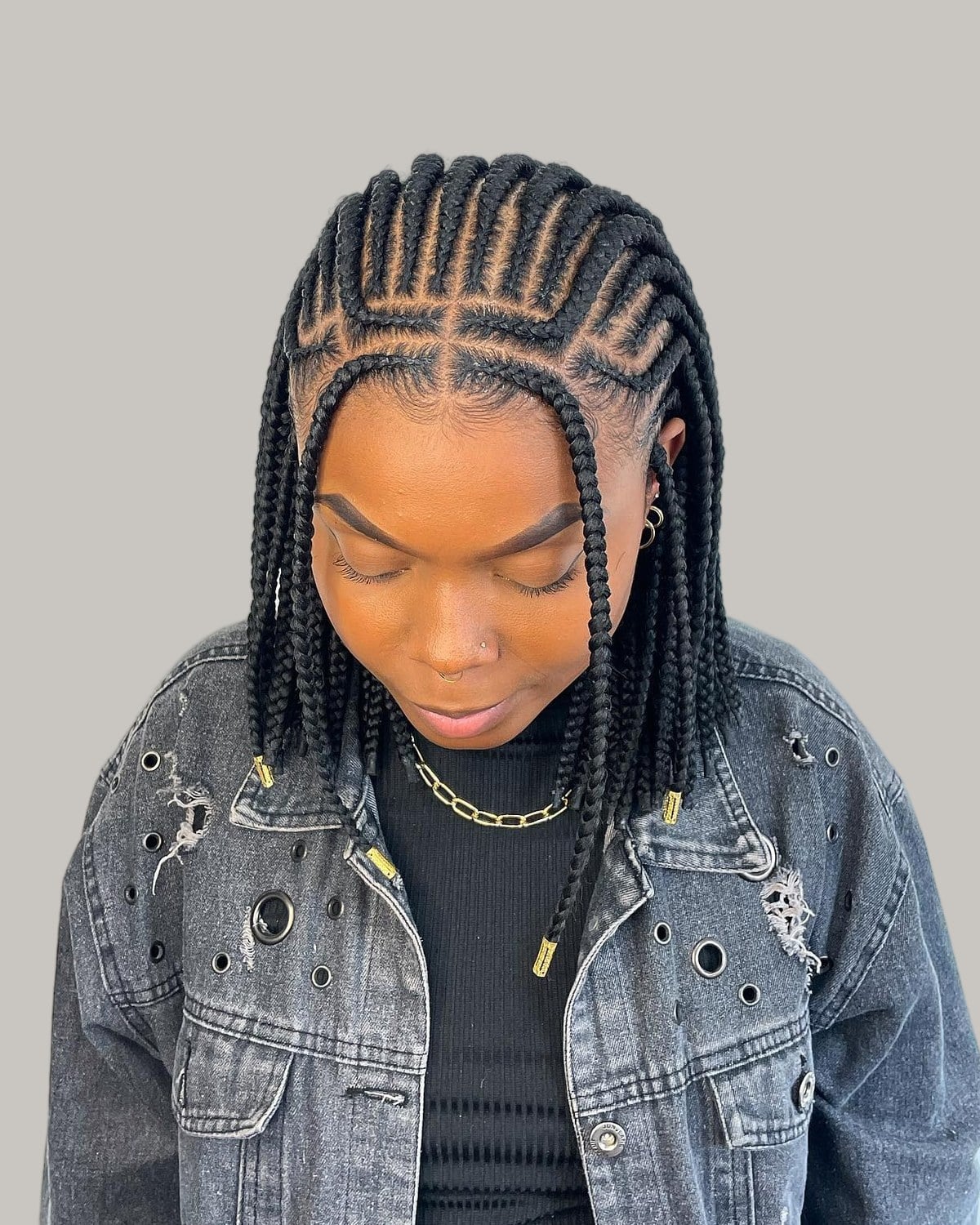 Woman in a denim jacket looking down, black Fulani braid bob with a center part