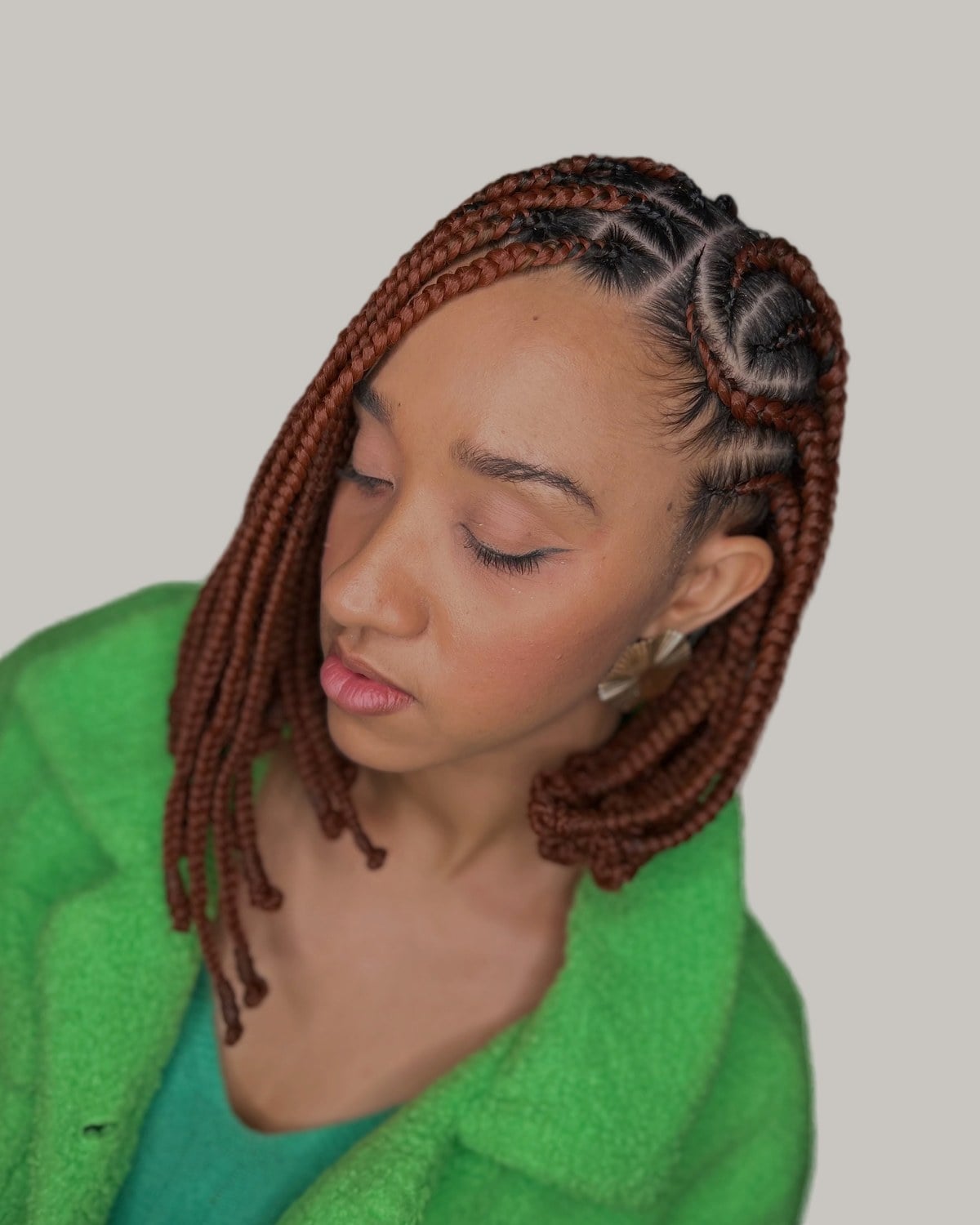 Woman in a green fleece jacket looking down, copper Fulani braid bob