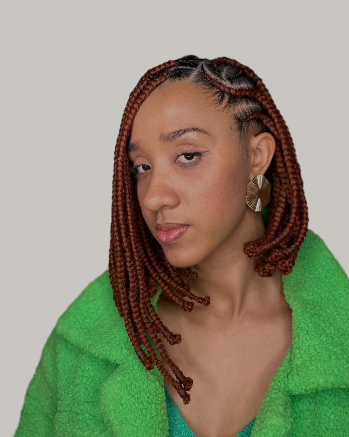 Woman in a green fleece jacket with a copper Fulani braid bob and gold earrings