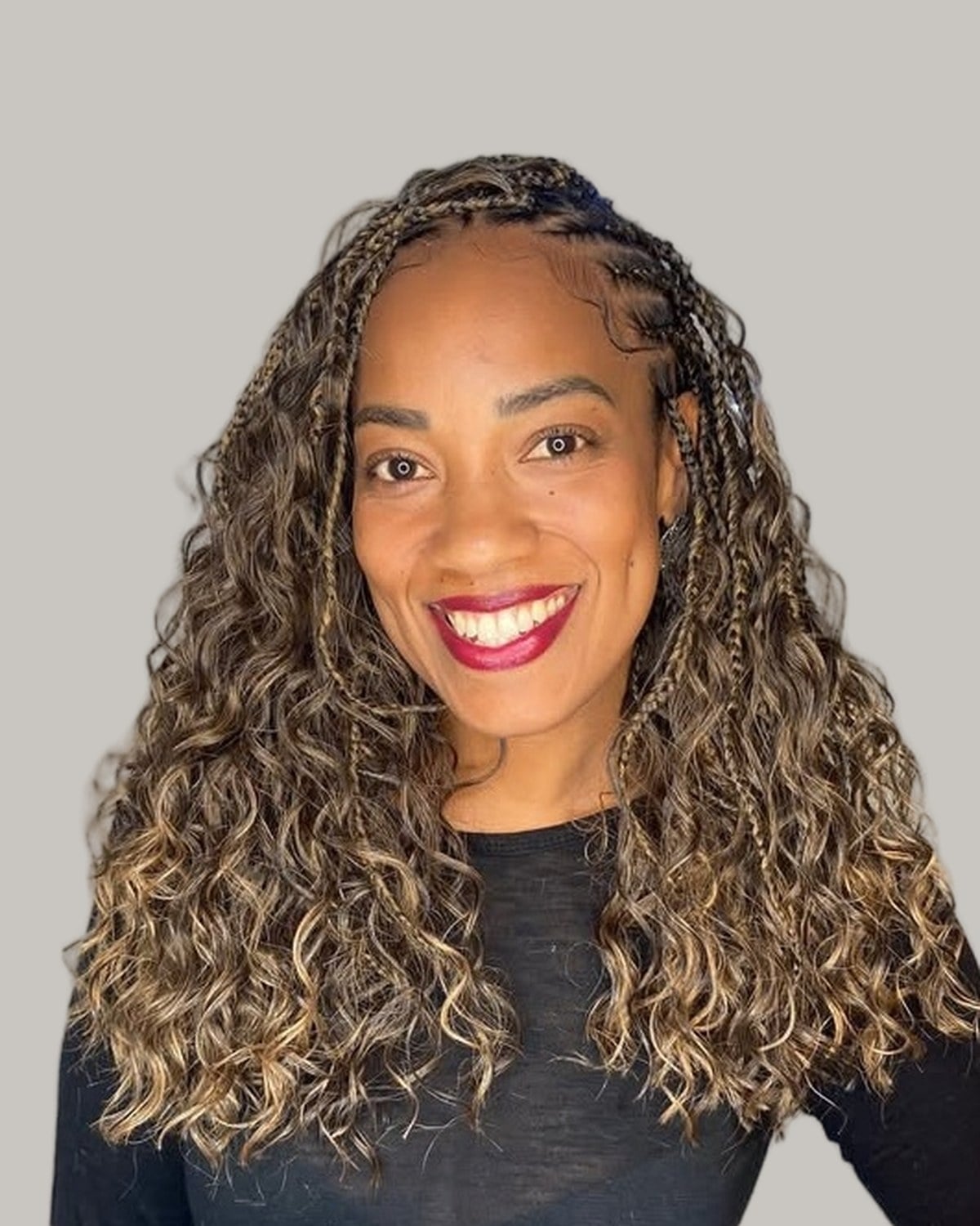 Smiling woman in a black top with flip-over Fulani braids and highlighted curls