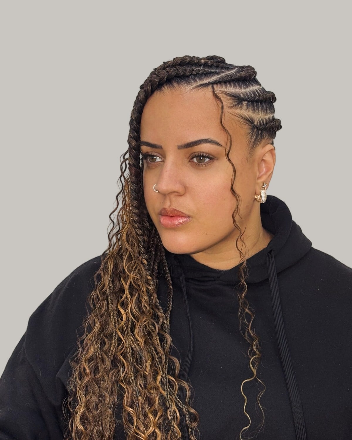 Woman in a black hoodie in three-quarter view, Fulani rows and curly braids with honey streaks