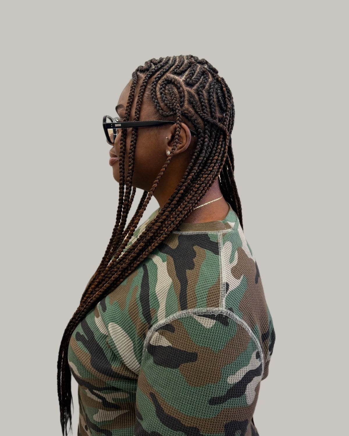 Woman in glasses and a camouflage top seen in profile with long Fulani braids