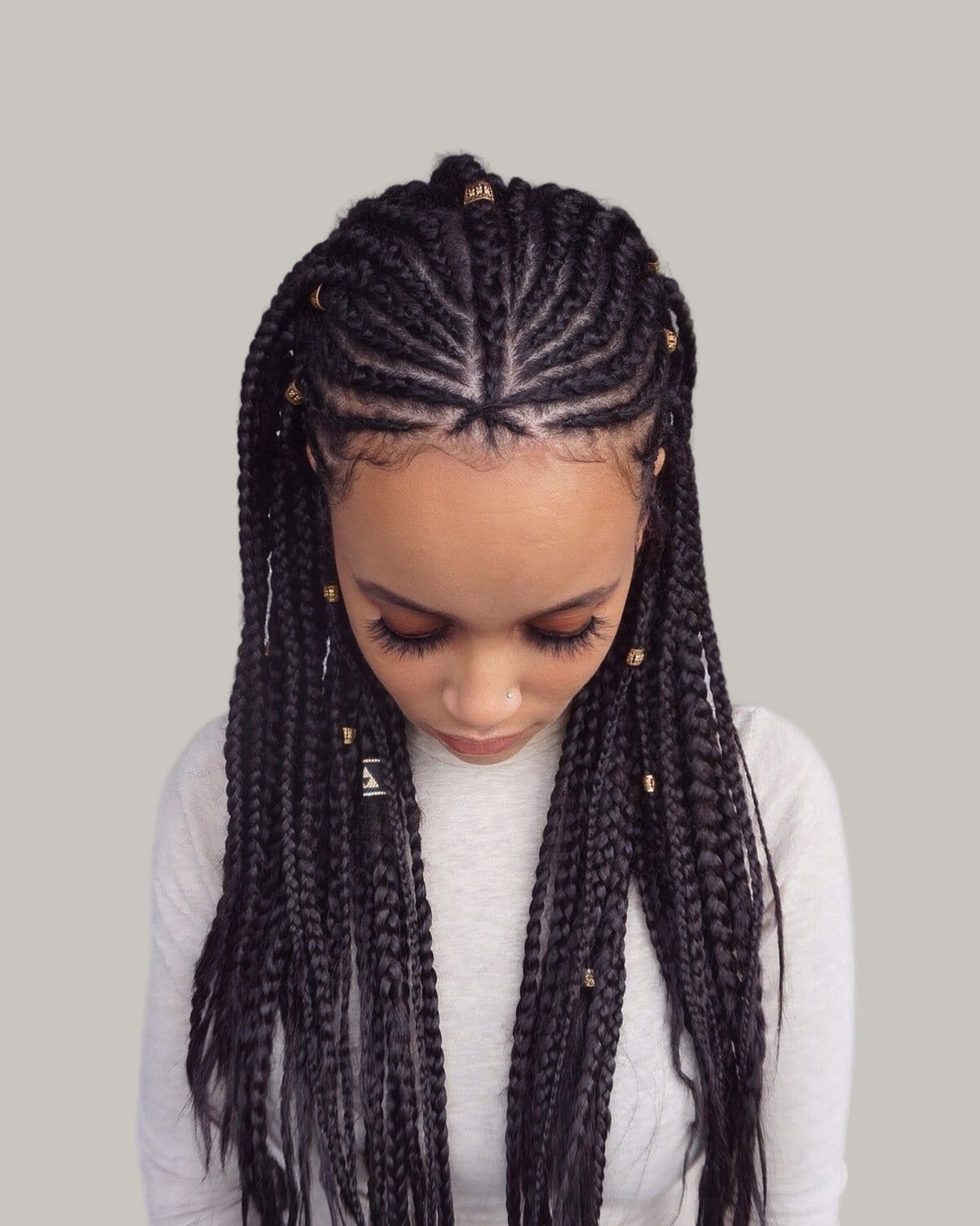 Woman in a cream top looking down, Fulani braids from a center part with small gold cuffs