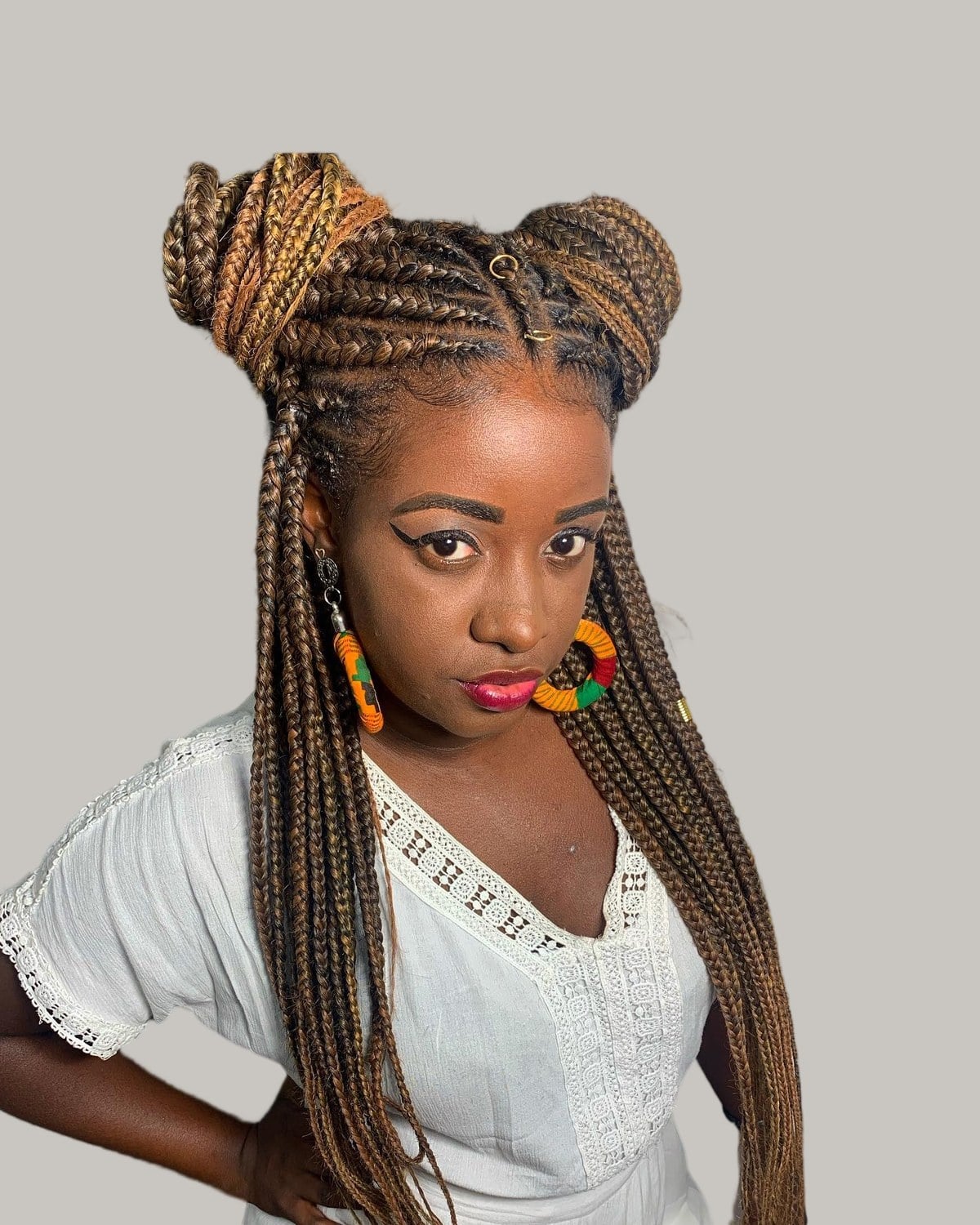 Woman in a white blouse looking at the camera, honey-brown Fulani braids and space buns