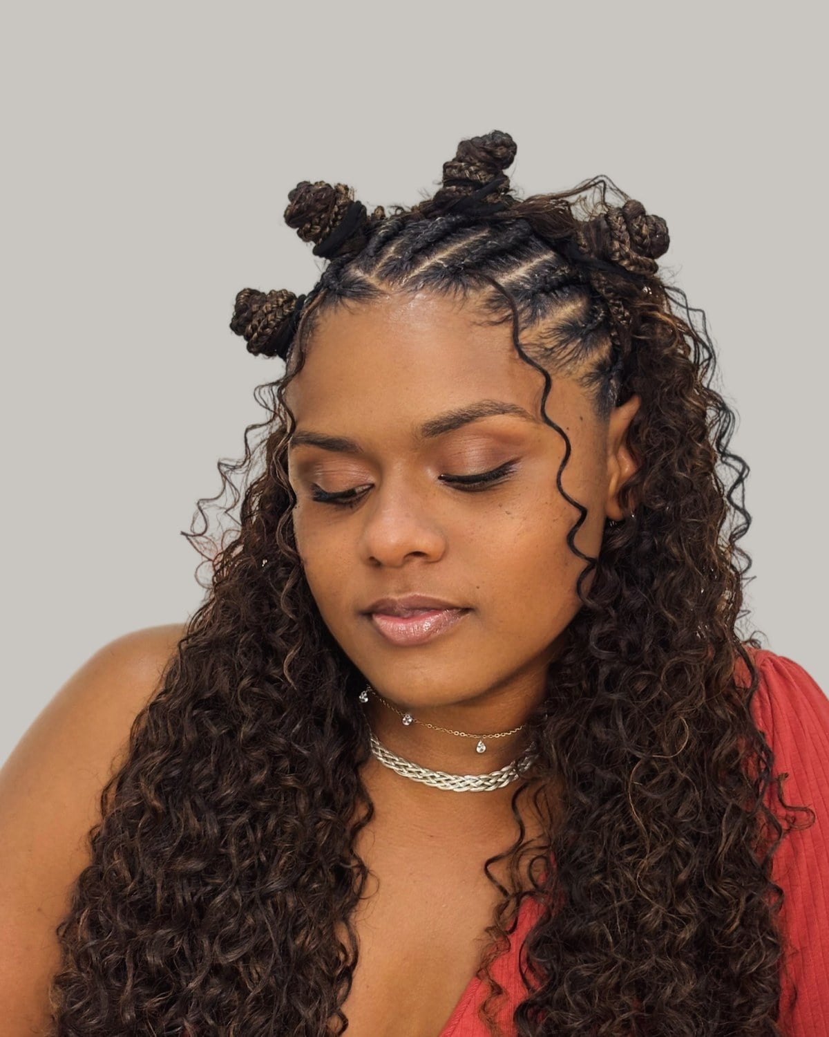 Woman in a red top looking down, half-up Fulani braids with buns and curls