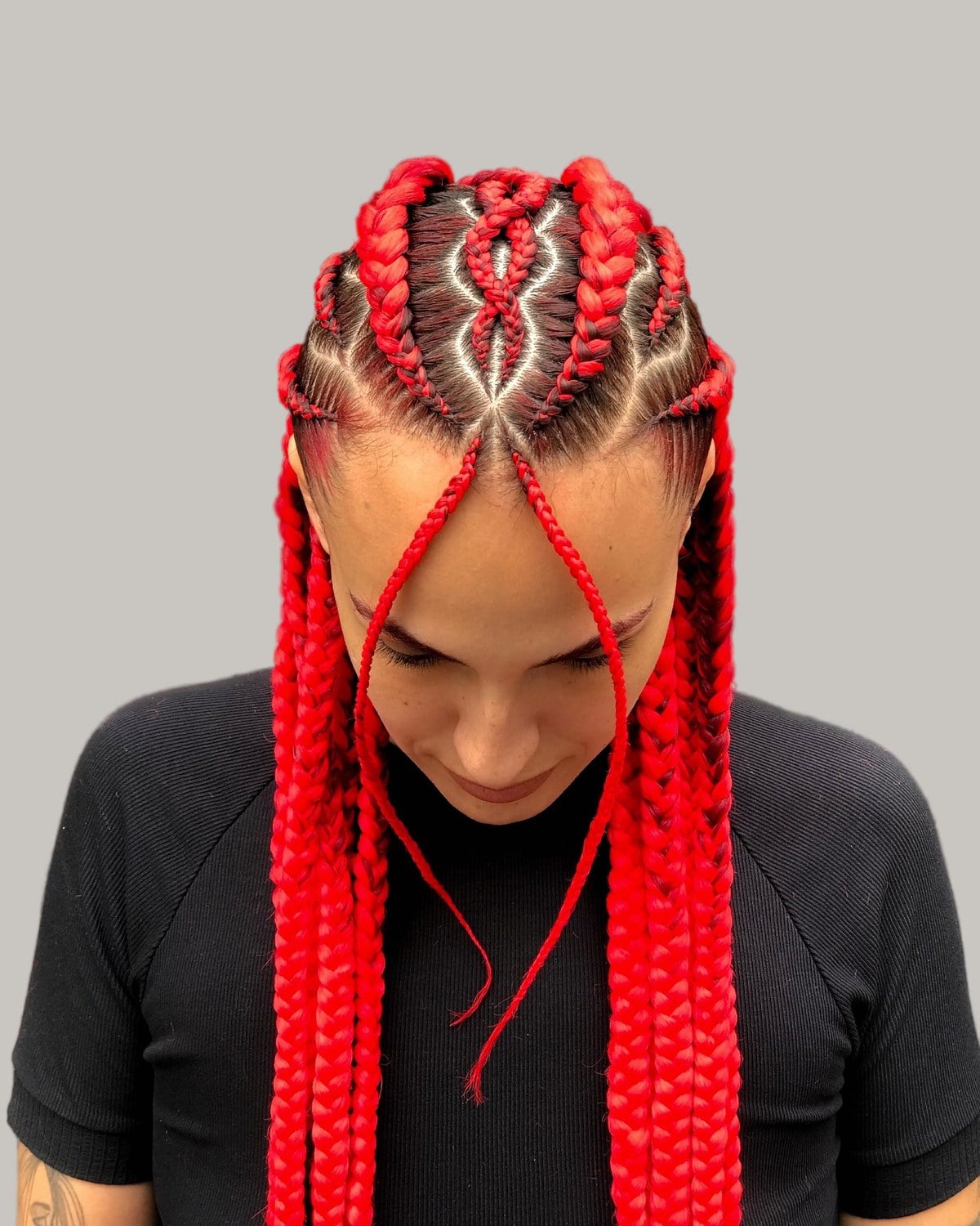 Woman in a black top looking down with bright red jumbo Fulani braids