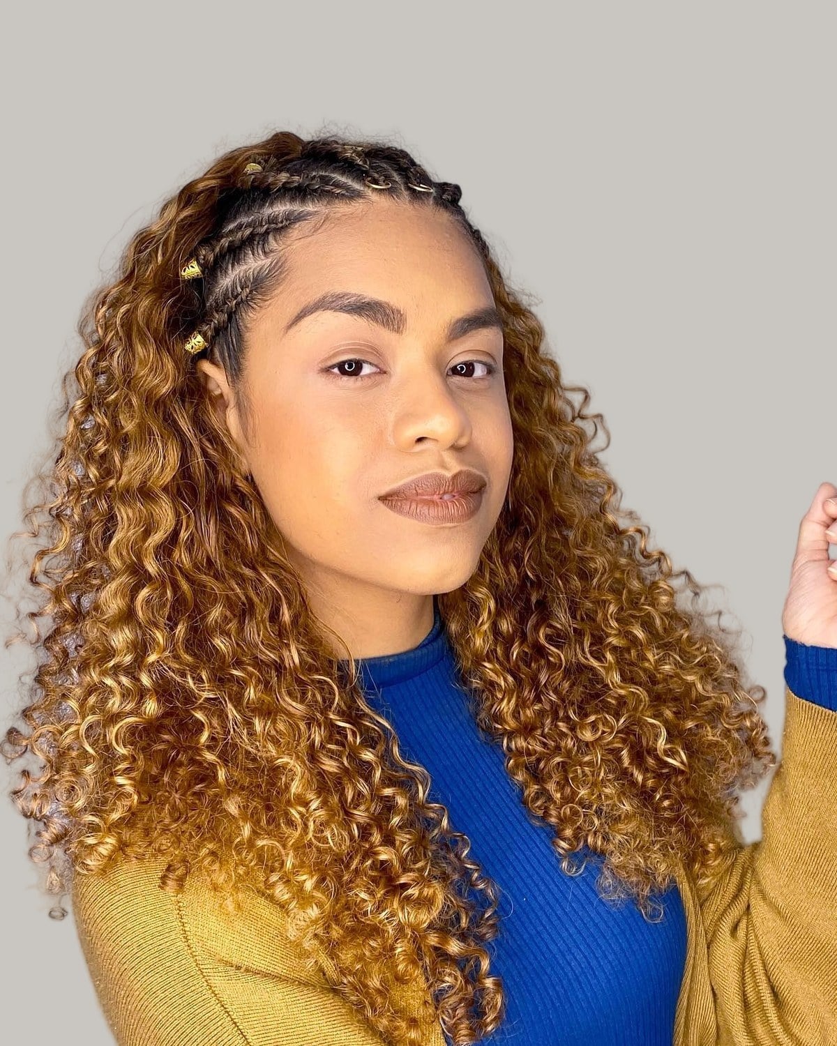 Woman in a blue top and mustard cardigan with Fulani cornrows and long golden curls
