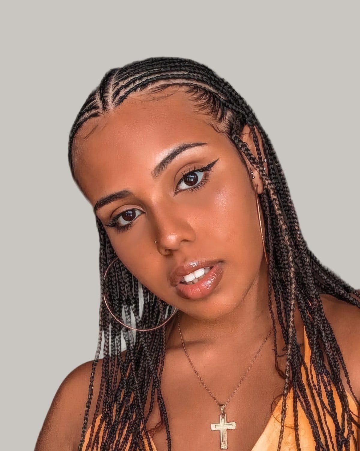 Woman in an orange top with small Fulani braids on her natural hair, rows from a center part