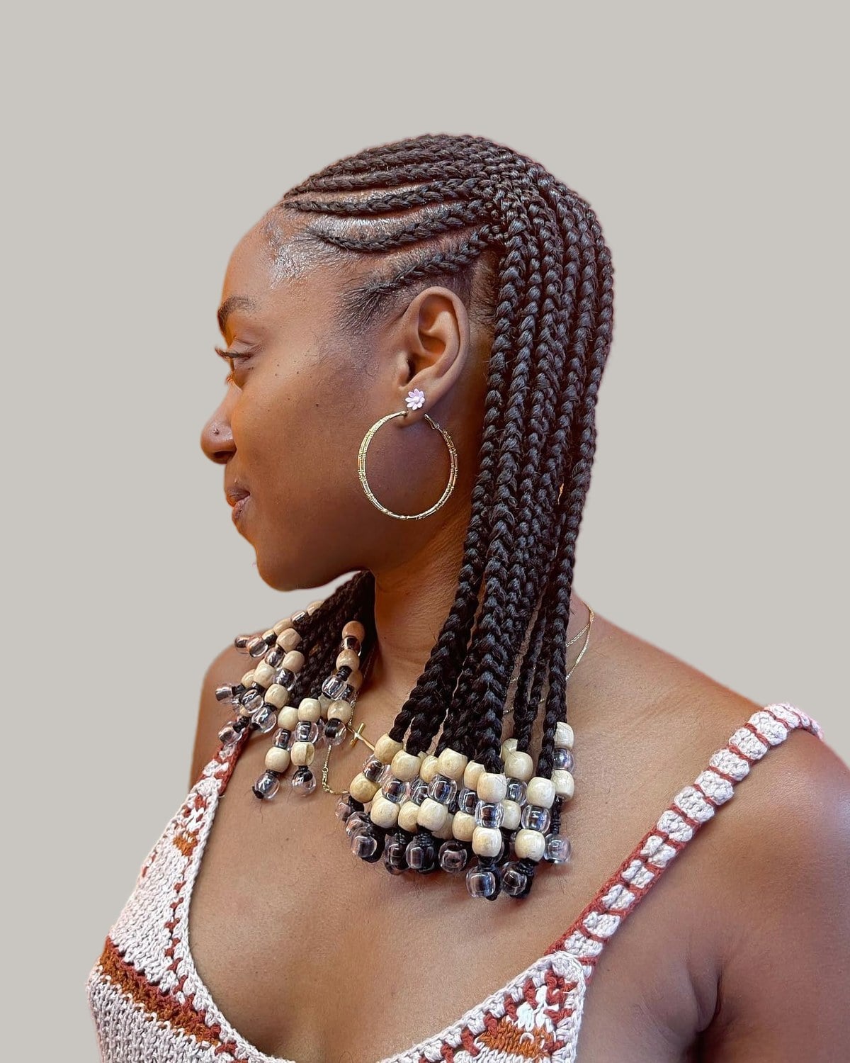 Woman in a white crochet top seen in profile, shoulder-length Fulani braids with beads