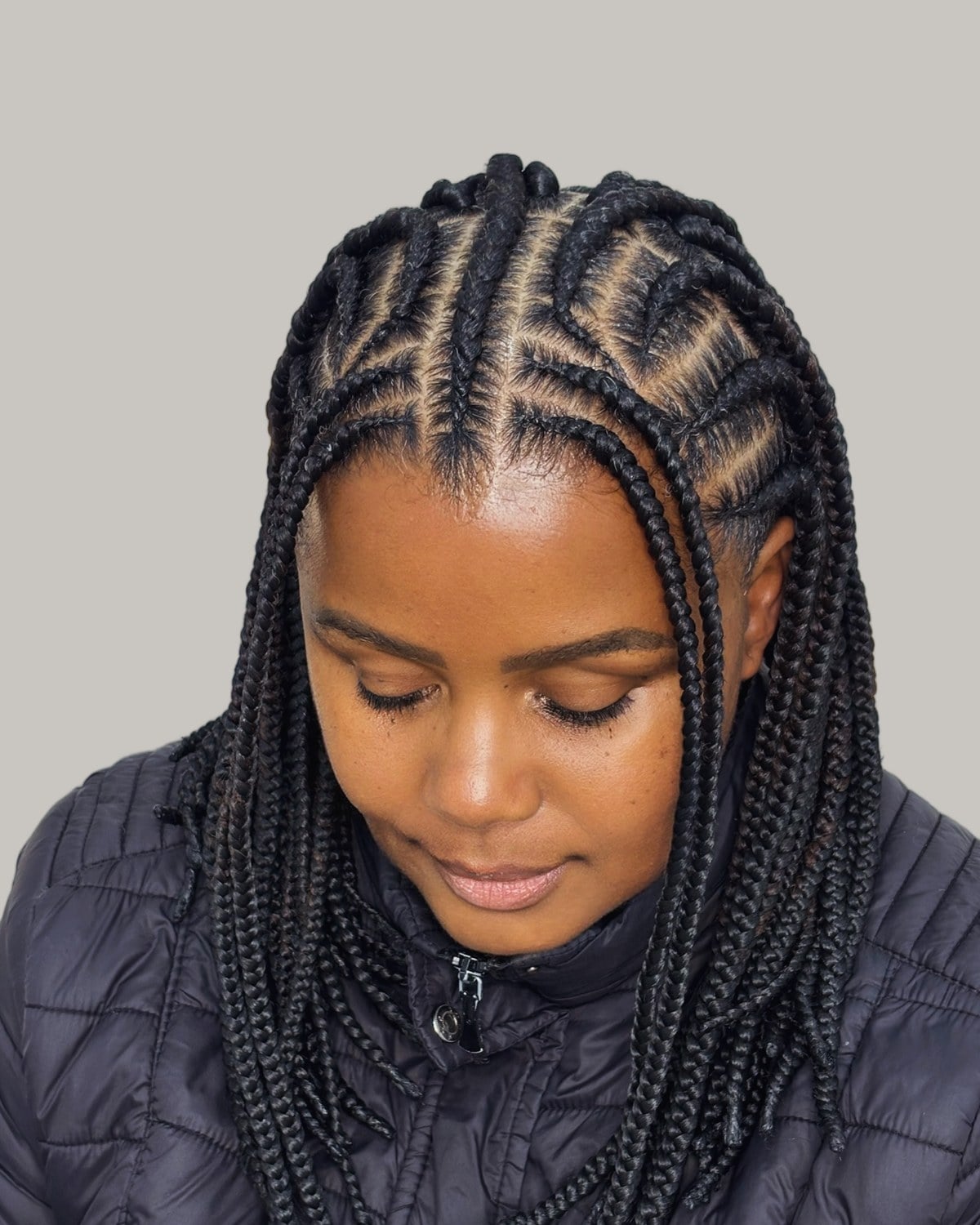 Woman in a black puffer jacket looking down, Fulani braids from a center part