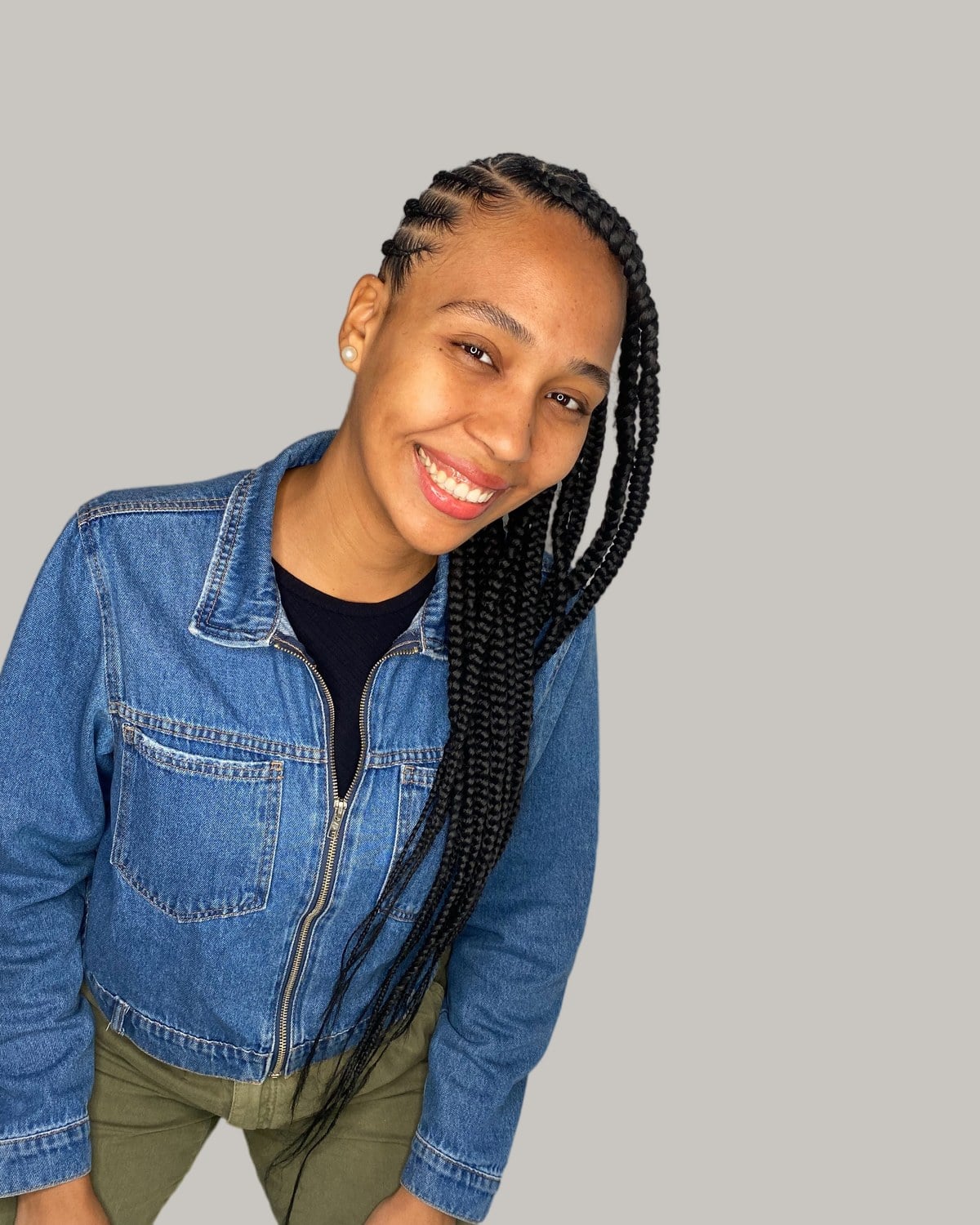 Woman in a denim jacket smiling, side-swept Fulani braids falling over one shoulder