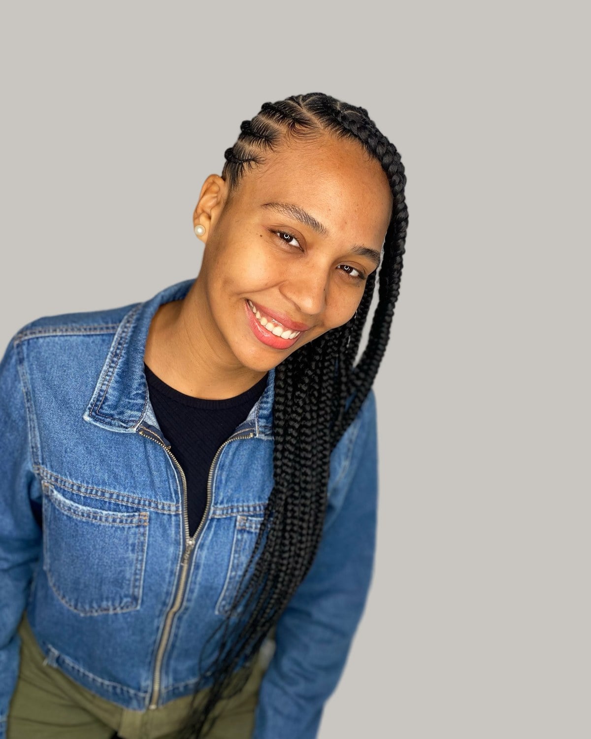 Smiling woman in a denim jacket with side-swept Fulani braids over one shoulder