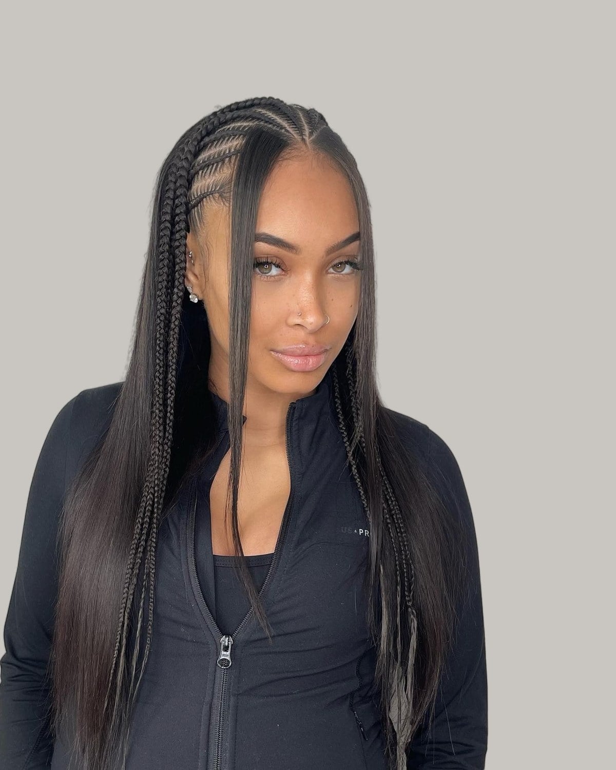 Woman in a black zip top in three-quarter view, side cornrows with long straight hair