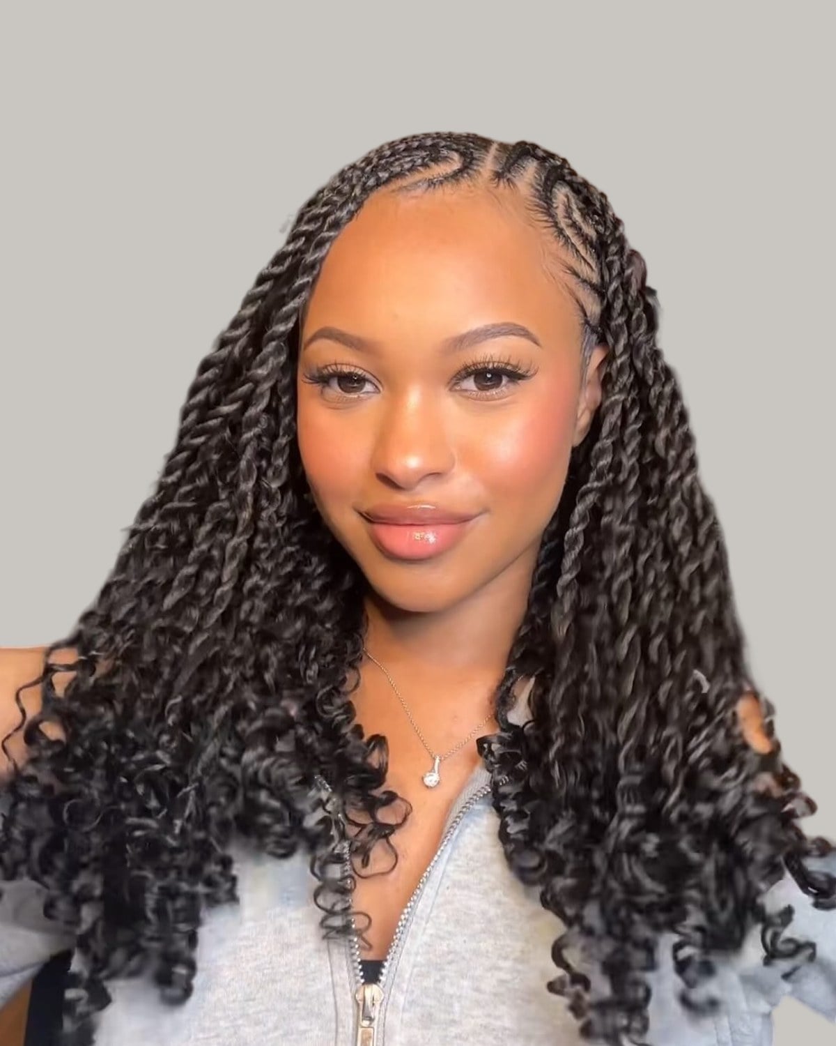 Woman in a gray zip top with Fulani cornrows and long twists with curly ends