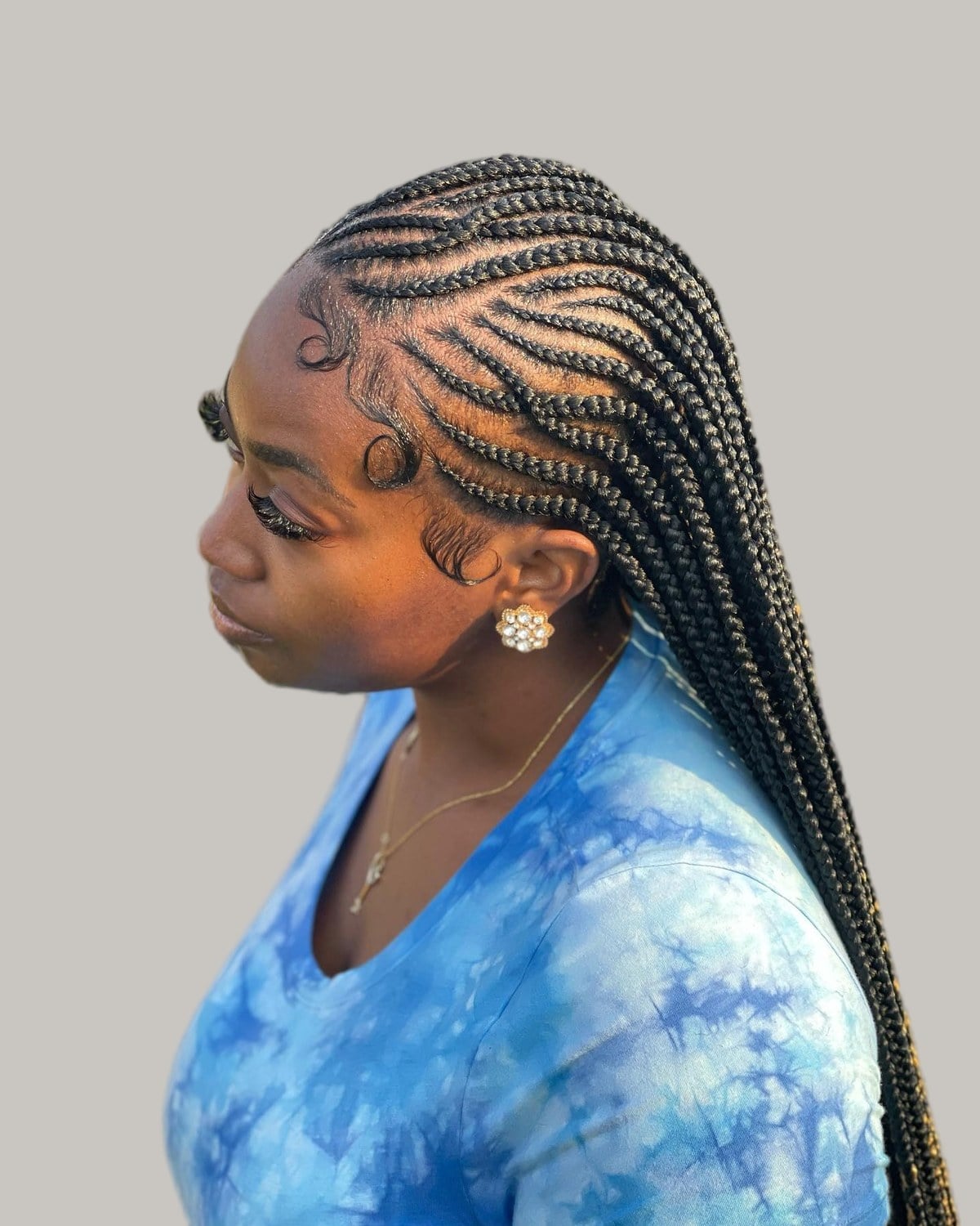 Woman in a blue tie-dye T-shirt looking down, black Fulani braids with curved side rows